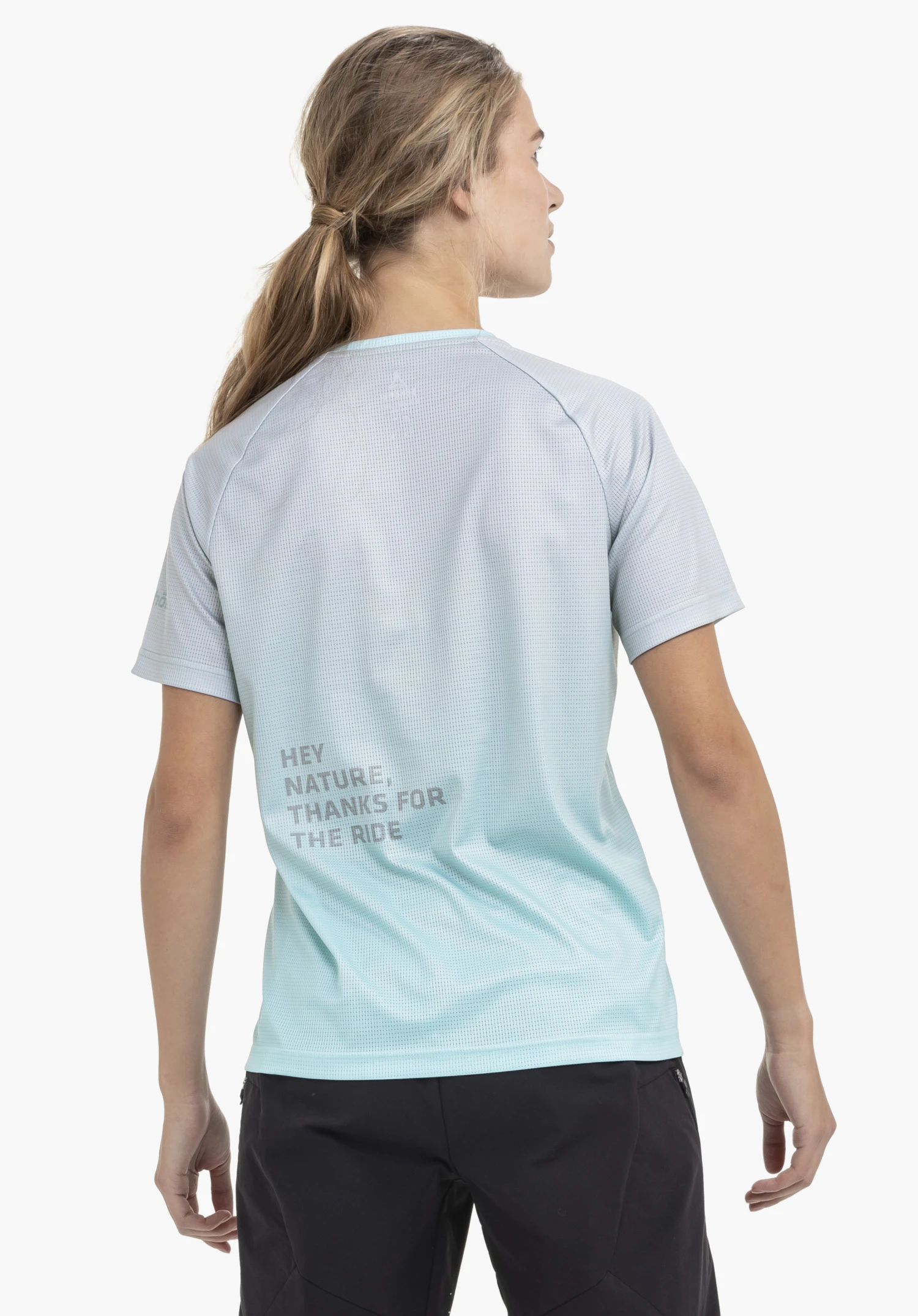 Shirt Style Koitere WMN in Blau. Das Model präsentiert sich in der Rückenansicht vor einem neutralen Hintergrund. Der hochwertige Stoff in Blau wird durch den reflektierenden Aufdruck ergänzt, während das dezente Schöffel-Logo auf dem Ärmel die sportliche Optik abrundet.