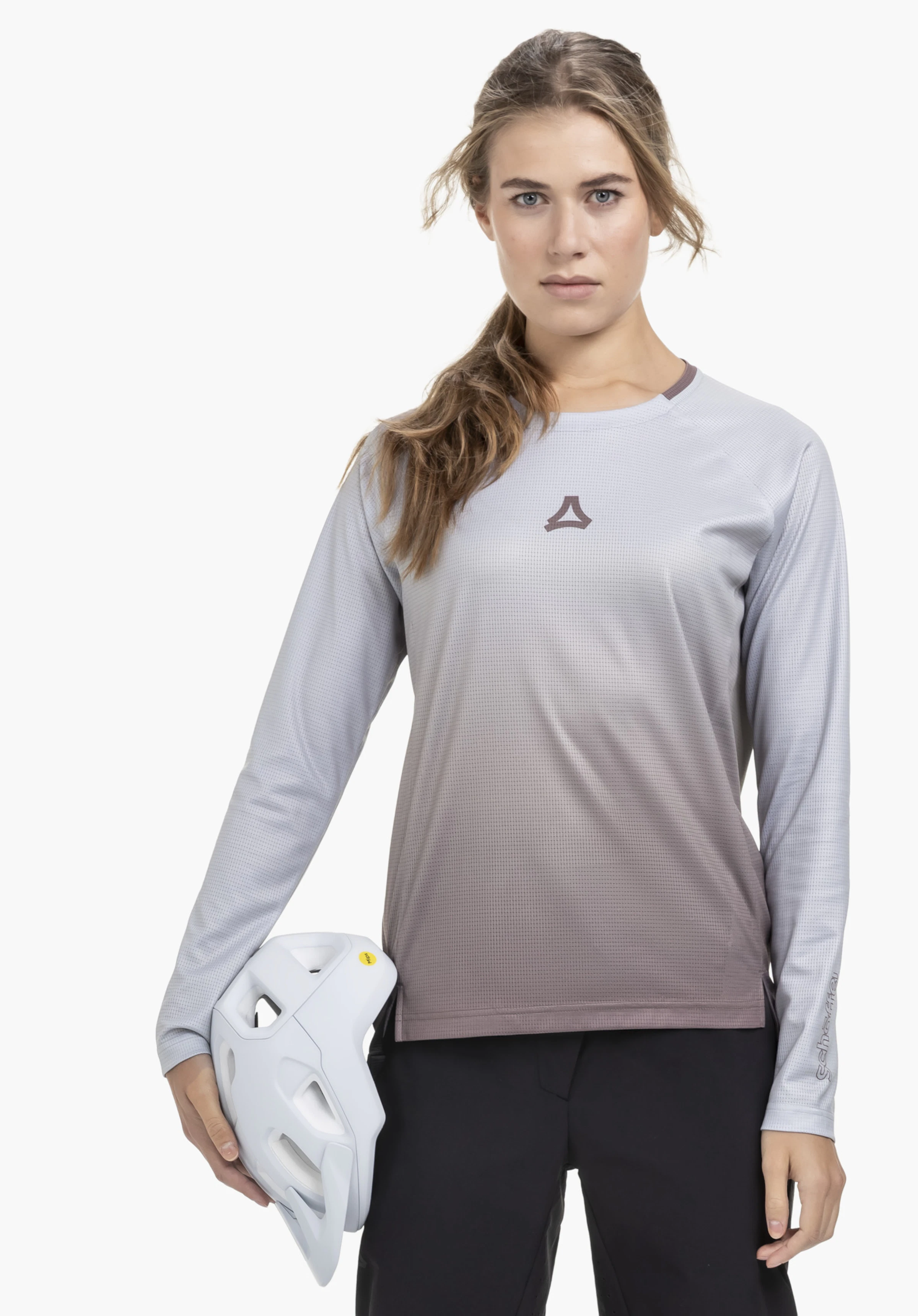 Longsleeve Style Koitere WMN: Eine Frau steht frontal vor einem neutralen Hintergrund und trägt das Longsleeve in lila. Das Shirt zeigt ein dezentes Schöffel-Logo auf der Brust und am Ärmel, während die Frau einen weißen Fahrradhelm in der Hand hält.
