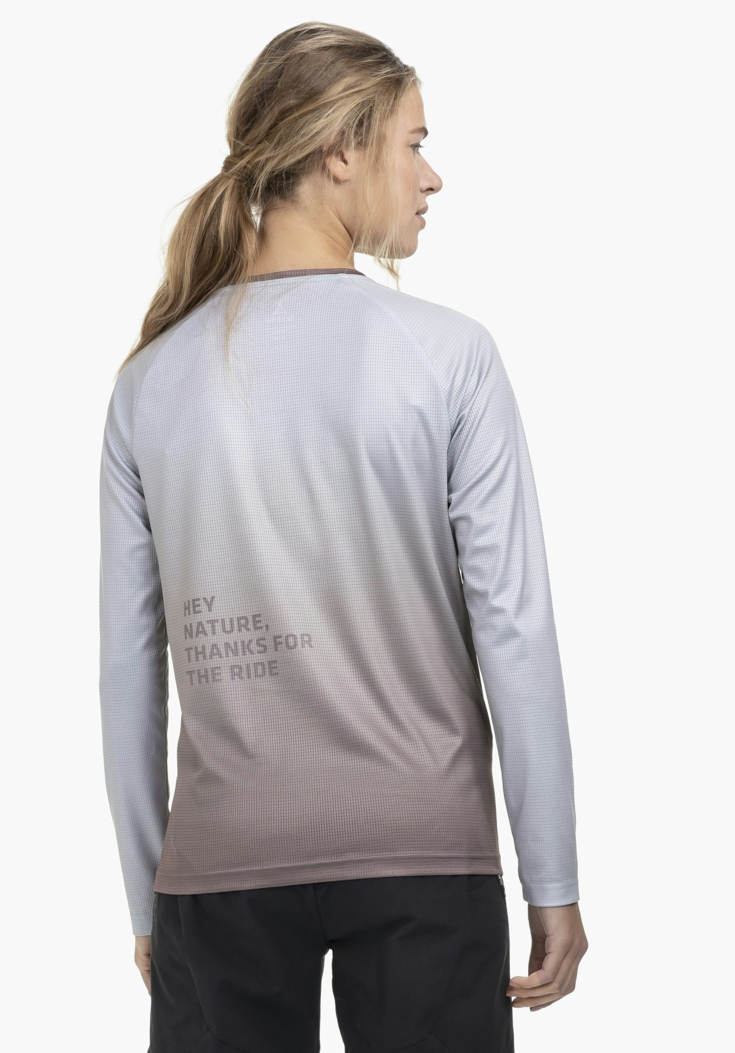 Longsleeve Style Koitere WMN in lila tegen een neutrale achtergrond: Het model is van achteren te zien, waarbij de subtiele opdruk en het kleurverloop benadrukt worden, terwijl ze licht over haar schouder kijkt.