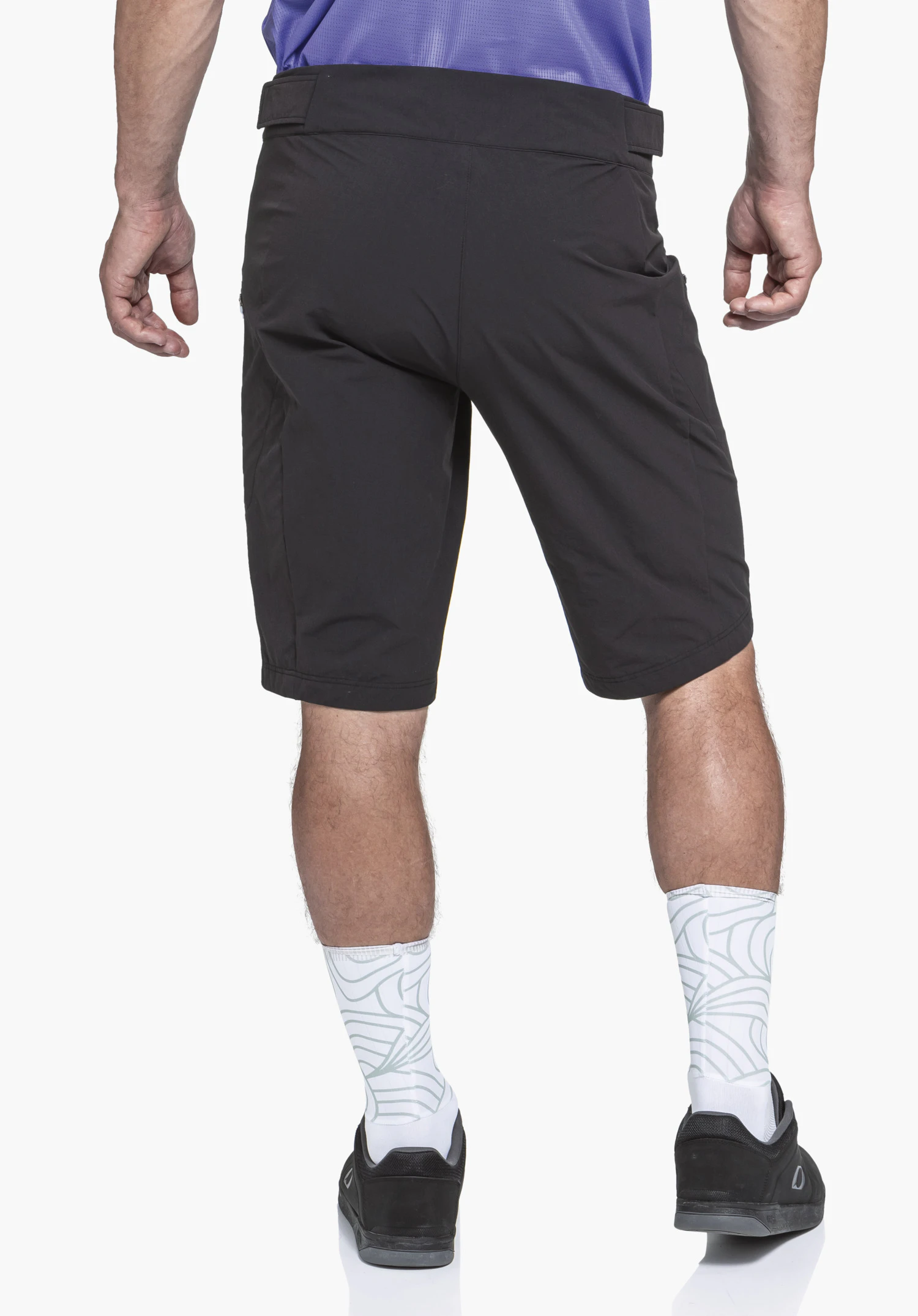 Shorts Style Puula MNS black shorts covering hips and thighs, worn by a standing person; white background, lilac shirt edge visible, white socks with light green pattern and black shoes.