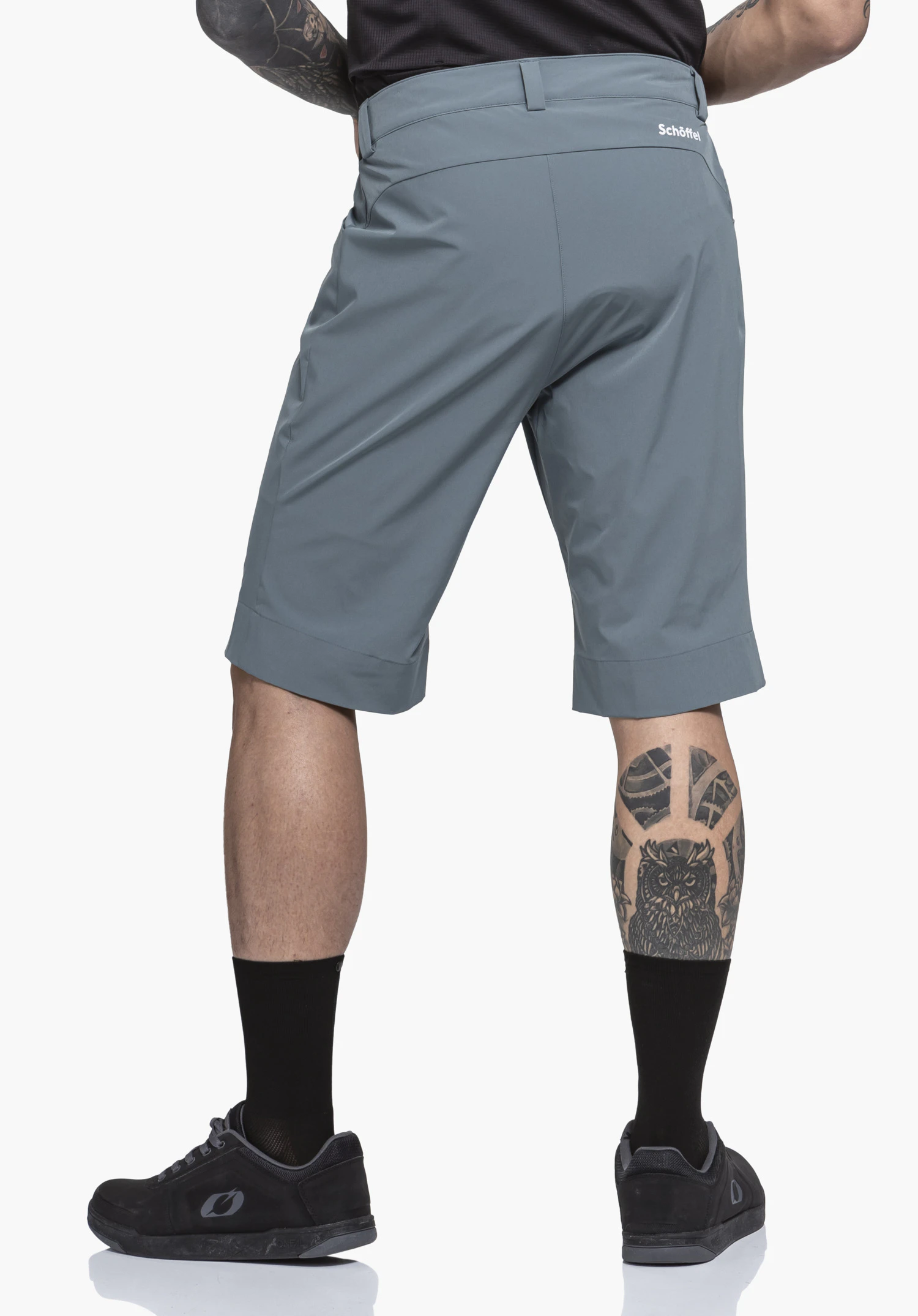 Shorts Style Puula MNS zwarte shorts bedekken heupen en dijen, gedragen door een staande persoon; witte achtergrond, lila shirt zichtbaar, witte sokken met lichtgroen patroon en zwarte schoenen.
