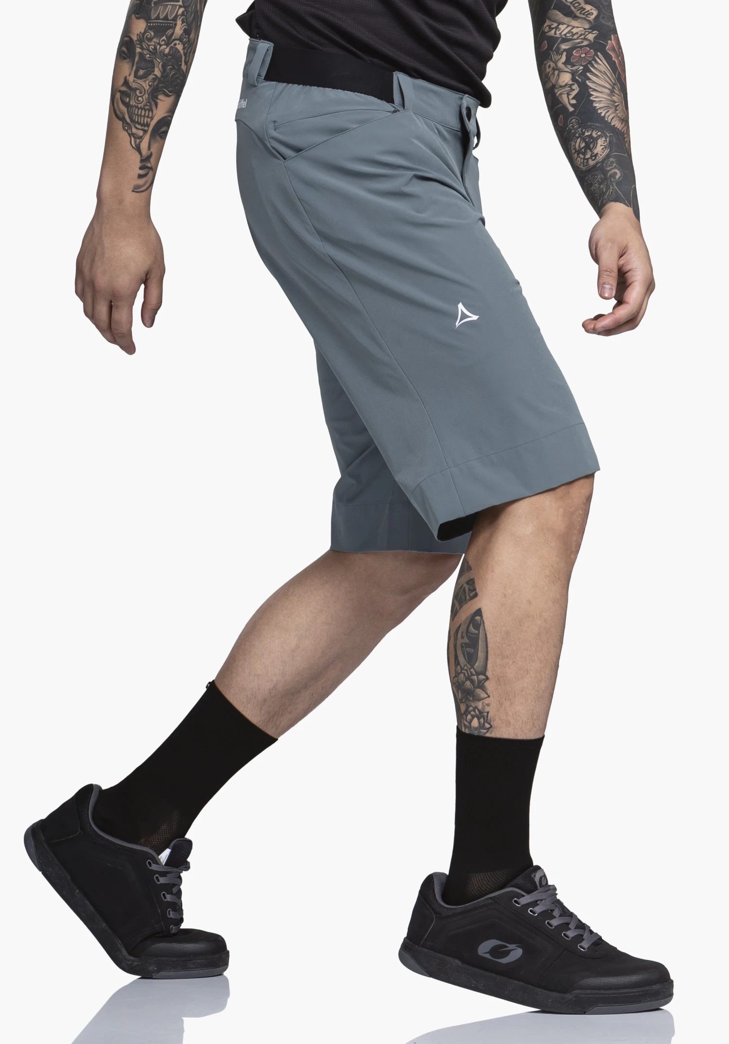 Shorts Style Keitele MNS donkerblauwe shorts, gedragen tijdens het lopen; context: model met getatoeëerde armen en benen, zwarte sokken en schoenen voor een witte studioachtergrond. Schöffel-logo. Tekst: "Schöffel".