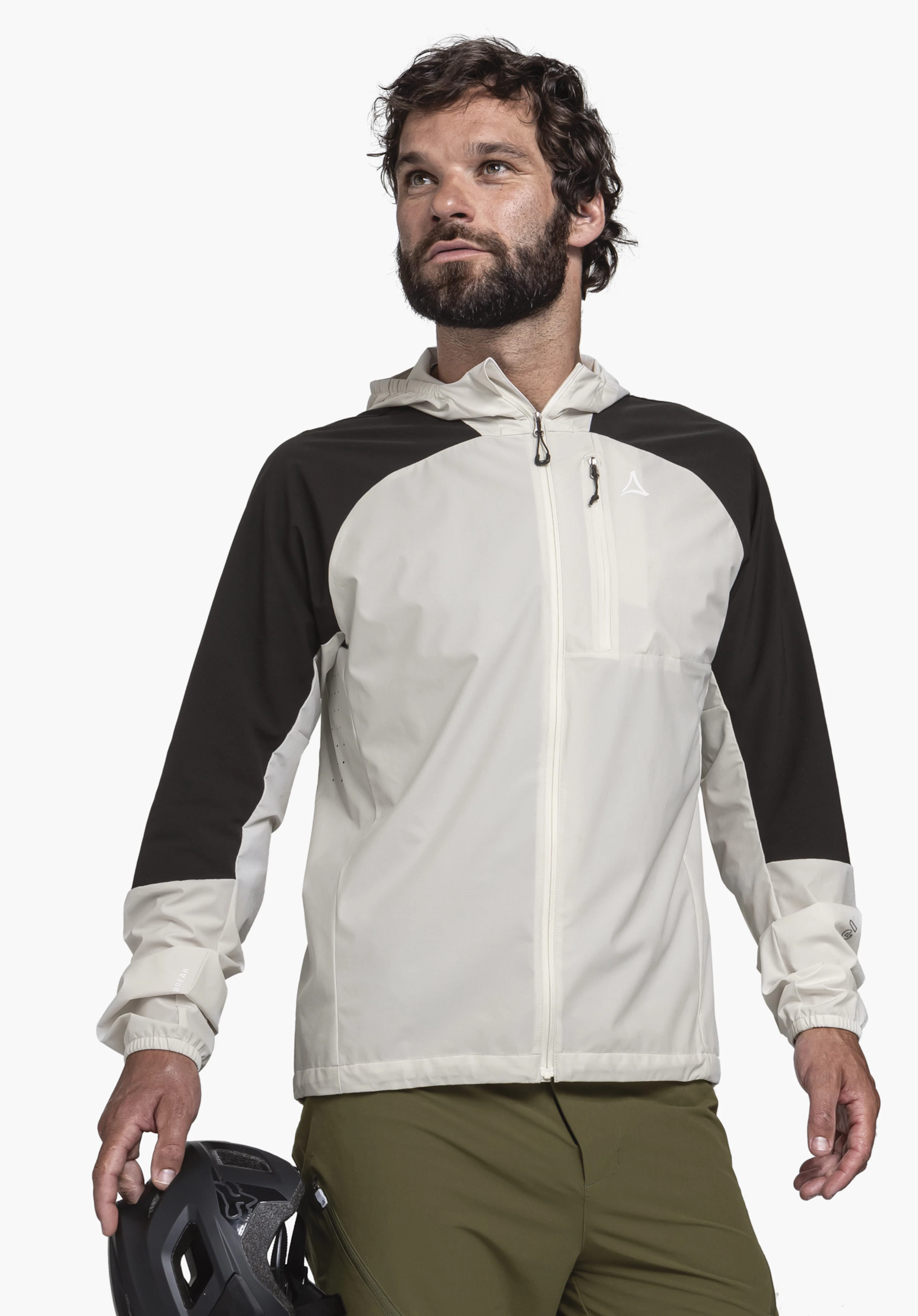 Hybrid Jk Style Mamry MNS. Ein Model steht frontal vor einem neutralen Hintergrund und präsentiert die Jacke in der Farbe natur mit kontrastierenden schwarzen Ärmelpartien. In der Hand hält das Model einen Fahrradhelm. Das Schöffel-Logo ist auf der linken Brust gut sichtbar.