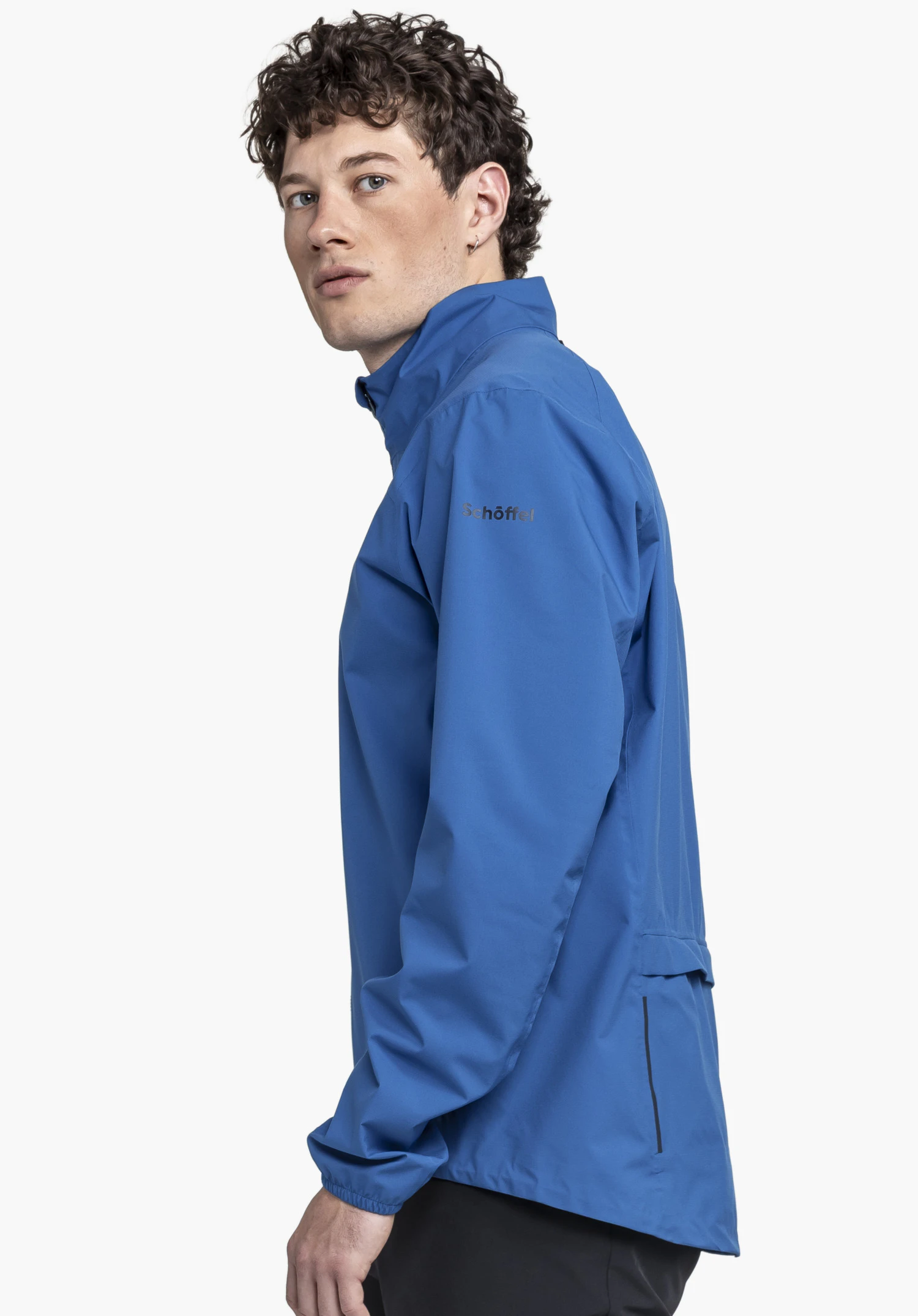 Jacket Style Lurbek MNS in Blau. Ein Model steht im Profil vor einem neutralen Hintergrund und präsentiert die Jacke. Das dezente Schöffel-Logo ist gut sichtbar auf dem Ärmel platziert.