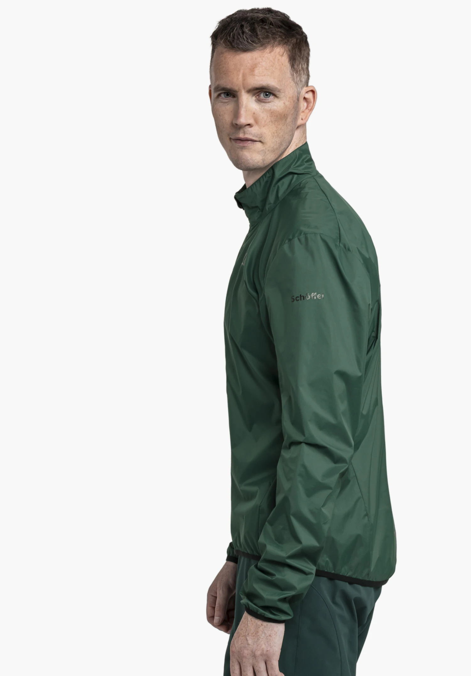 Jacket Style Cannobio MNS in green: The model is positioned in a side profile against a neutral background, looking directly at the camera. The subtle Schöffel logo on the upper arm accentuates the clean design of the jacket.
