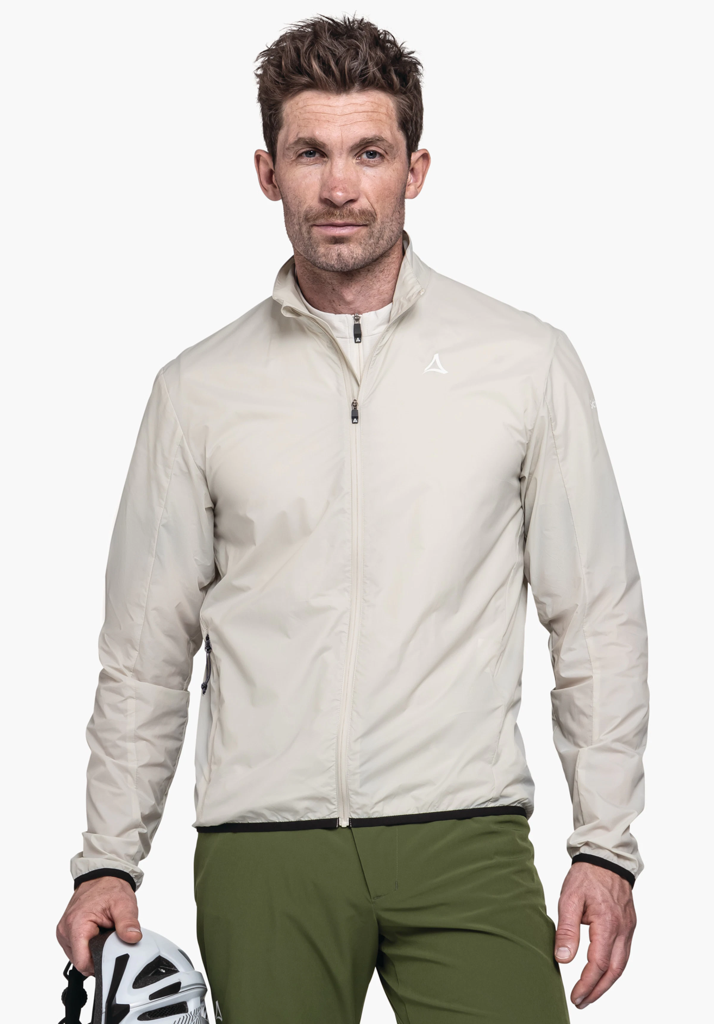 Jacket Style Cannobio MNS de couleur nature. Un mannequin se tient de face en portant la veste zippée, avec le logo Schöffel visible sur la poitrine gauche. Le mannequin tient un casque de vélo à la main devant un fond neutre.
