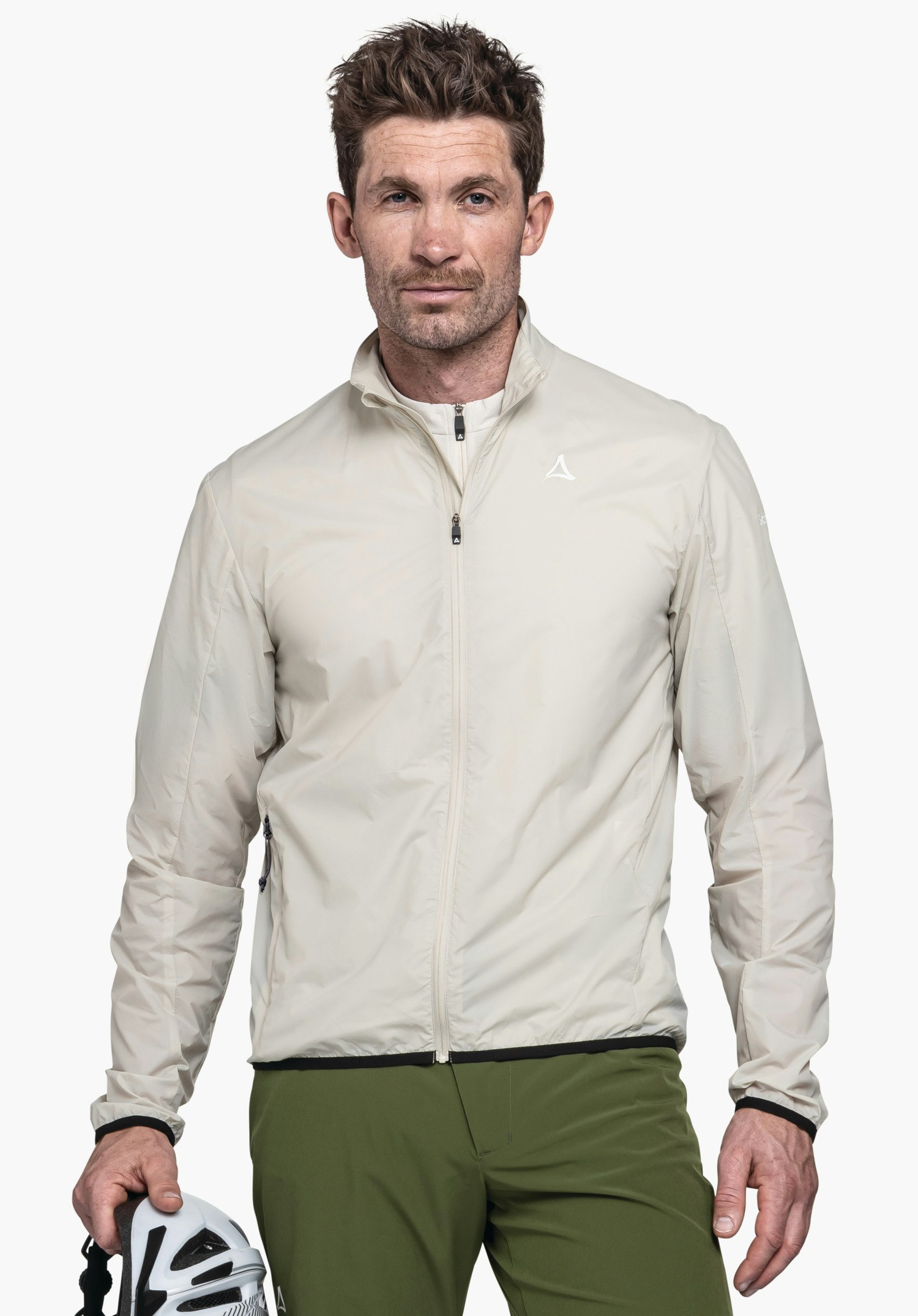 Jacket Style Cannobio MNS in der Farbe Natur. Ein Model steht in Frontalansicht und trägt die geschlossene Jacke, auf deren linker Brust das Schöffel-Logo zu sehen ist. In der Hand hält das Model einen Fahrradhelm vor einem neutralen Hintergrund.