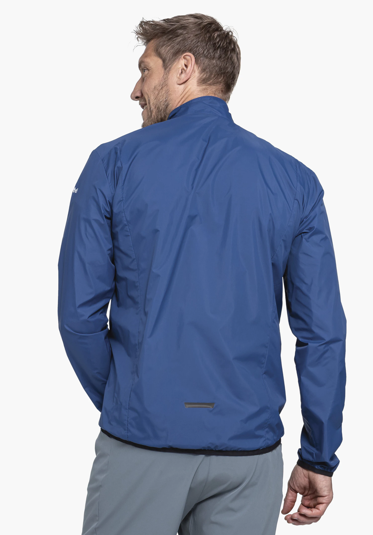 Jacket Style Cannobio MNS veste imperméable bleu foncé, portée par un homme, vue arrière; homme légèrement de côté devant un fond blanc, pantalon gris. Aucun texte visible.
