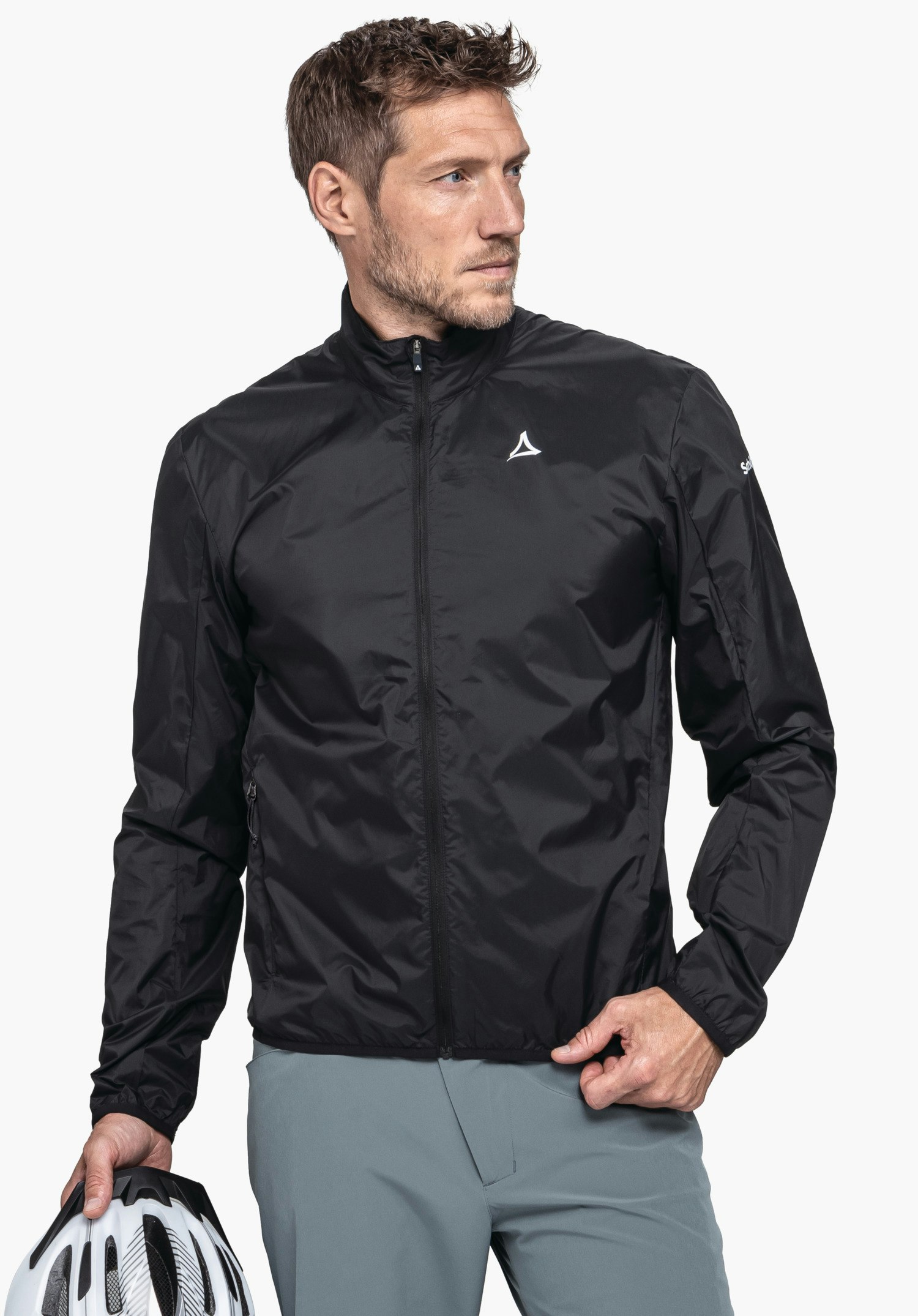 Jacket Style Cannobio MNS schwarze leichte Jacke mit Schöffel-Logo, zugezippt; Mann hält weißen Fahrradhelm, steht vor hellem einfarbigem Hintergrund. Text: Schöffel.