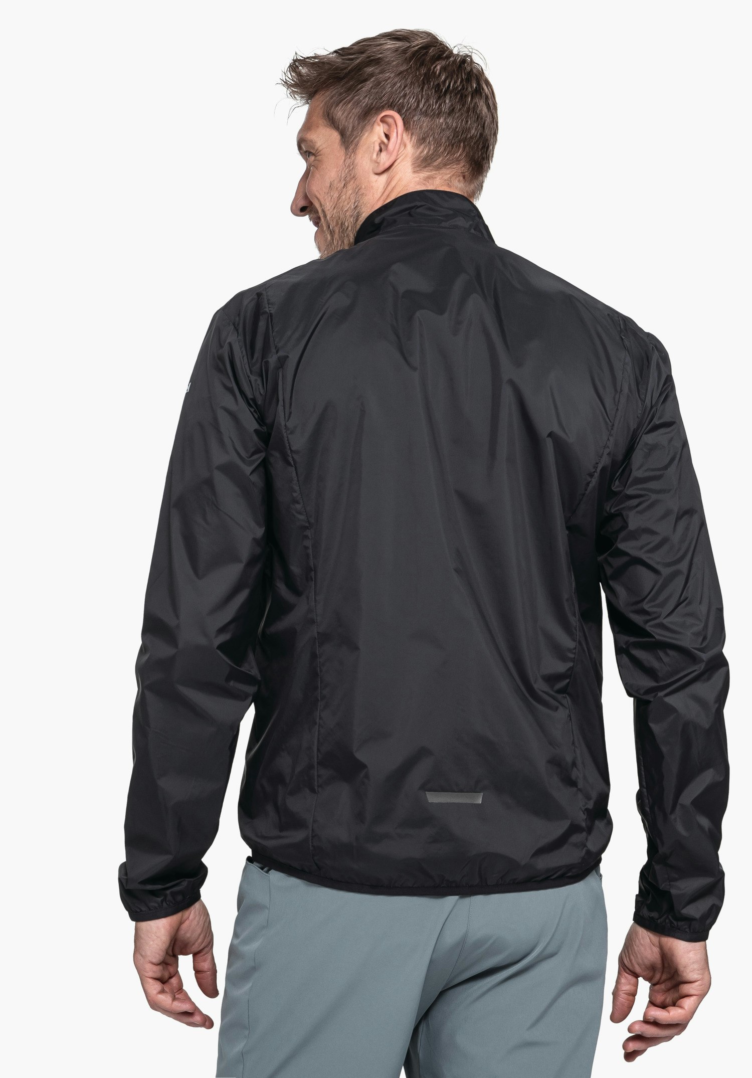 Jacket Style Cannobio MNS Jacke: dunkel schwarz, getragen von einem Mann, der rückwärts steht und über die Schulter blickt; sportliches, glattes Material; Kontext: hell weißer Hintergrund, Hose hell blau.
