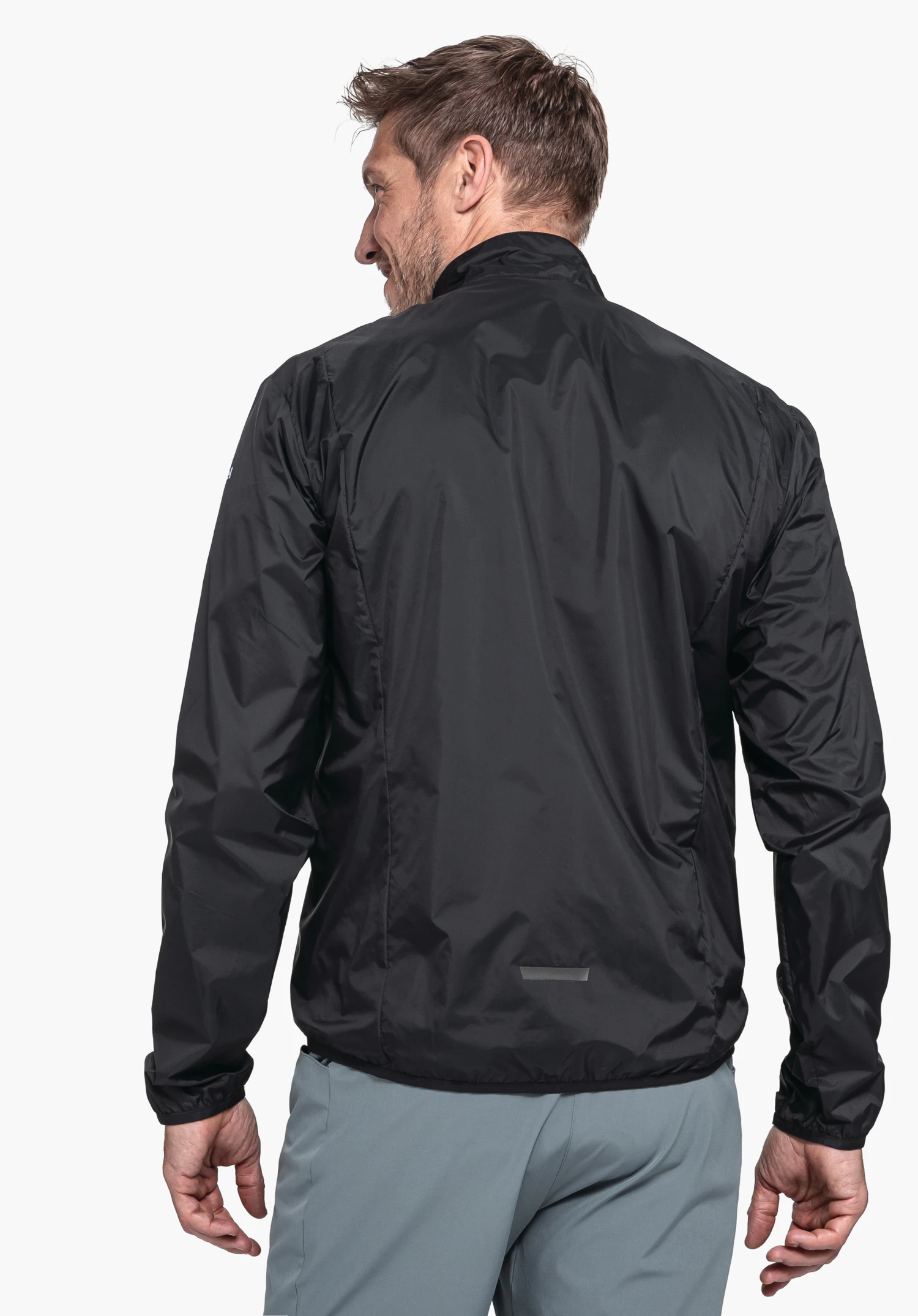 Jacket Style Cannobio MNS black jacket worn by a man standing with his back to the camera and looking over his shoulder; sporty, smooth fabric; light white background; light blue trousers.