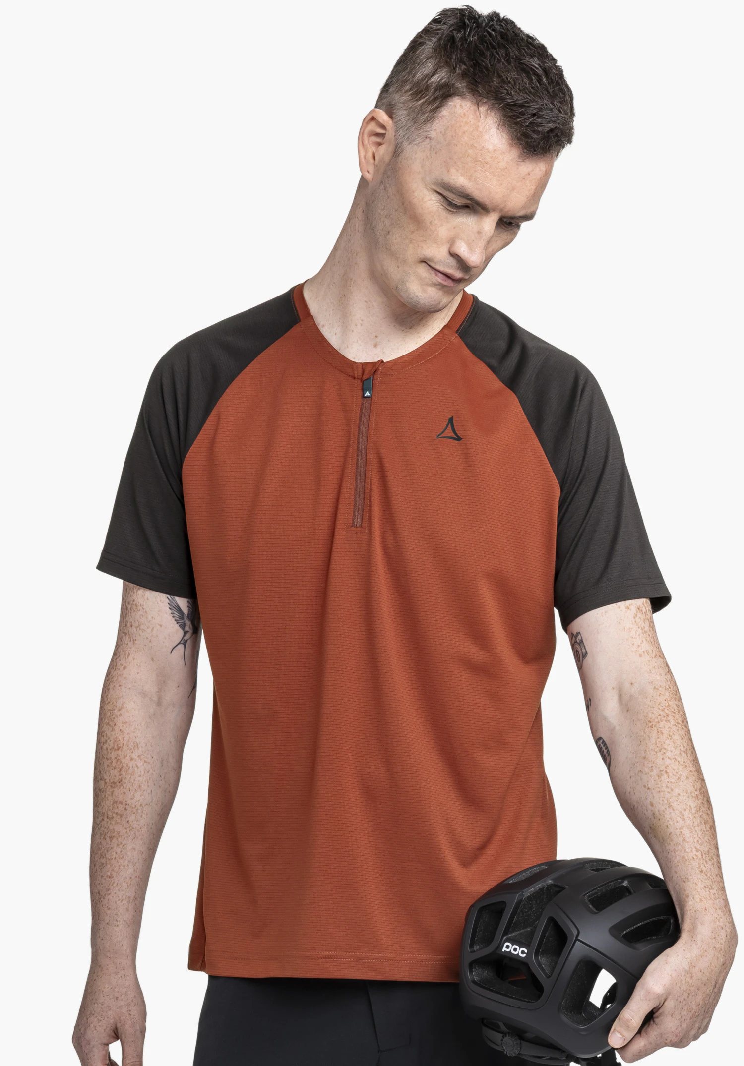 CIRC Shirt Style Wetluga MNS: Der Mann steht frontal zum Betrachter, blickt konzentriert nach unten und hält einen Helm in der Hand. Das Shirt in Rot mit dunklen Ärmeln präsentiert sich auf einem neutralen Hintergrund, wobei das diskrete Schöffel-Logo auf der Brust gut sichtbar ist.