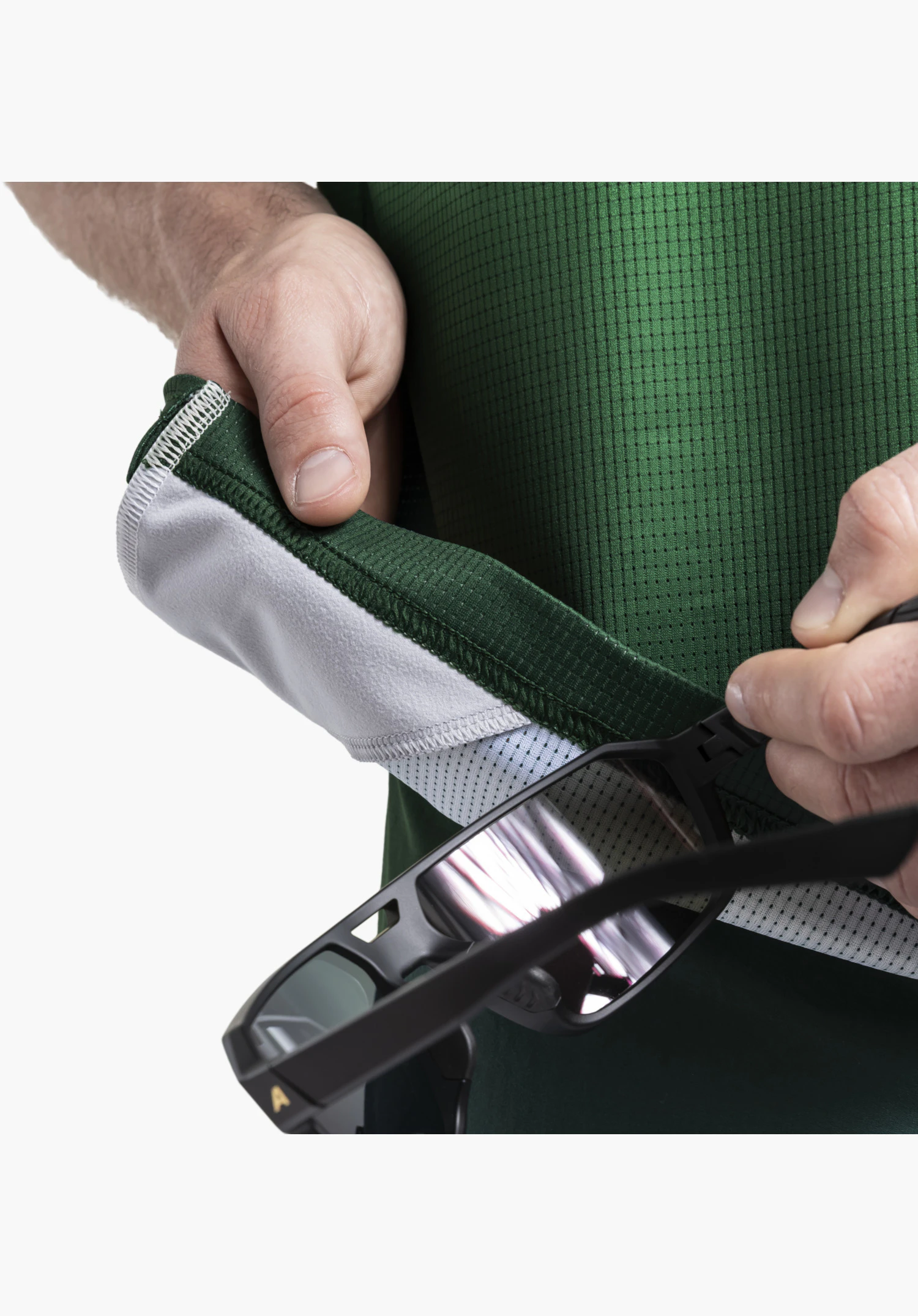 Shirt Style Koitere MEN, detail view of the practical glasses cleaning cloth on the inside of the green, textured fabric, being used to clean a pair of sunglasses, close-up in front of a white/neutral background.