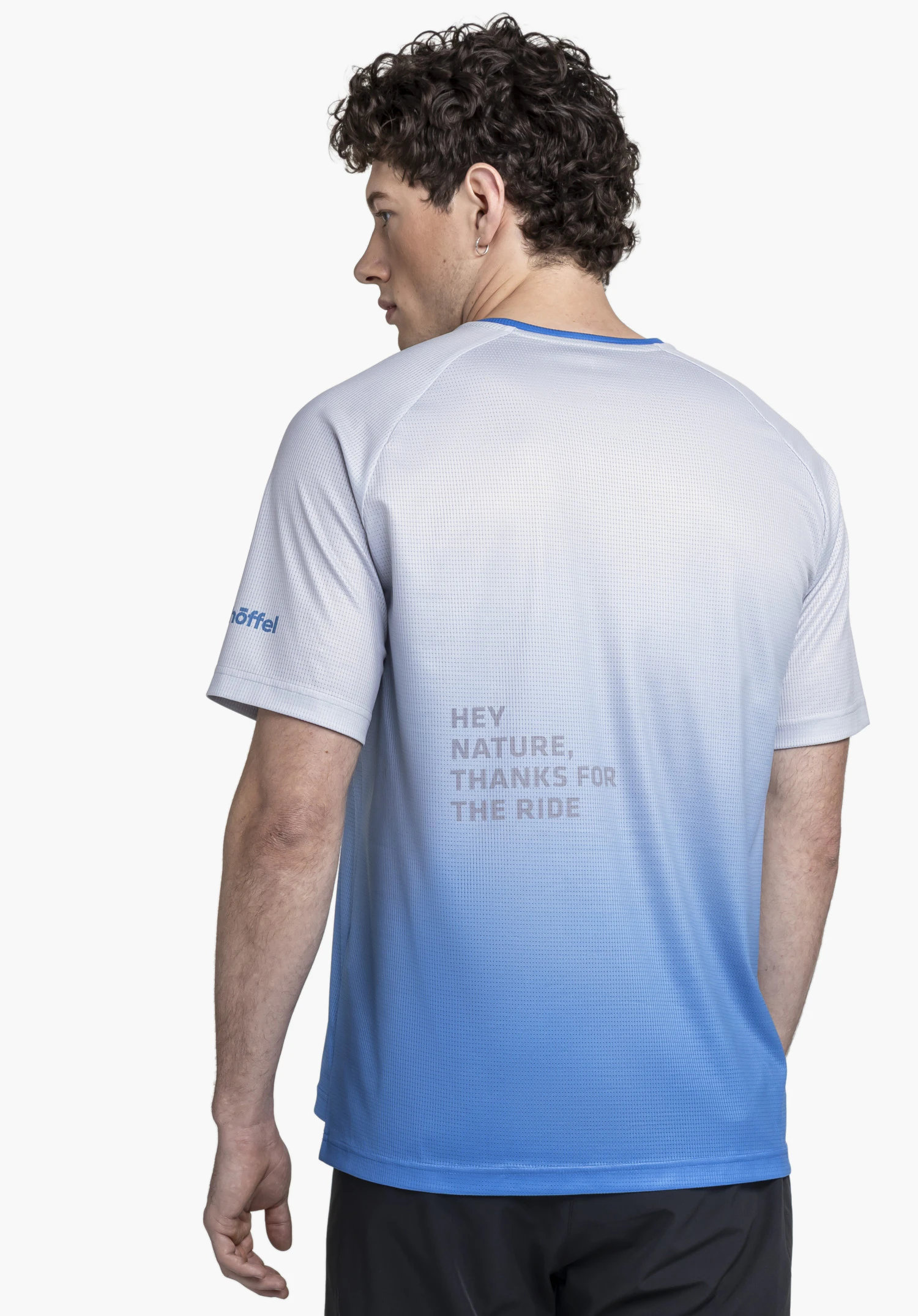 Shirt Style Koitere MEN is shown from the back against a neutral background. The model wears the blue technical shirt, which features the Schöffel logo on the sleeve and a motivational print on the back.
