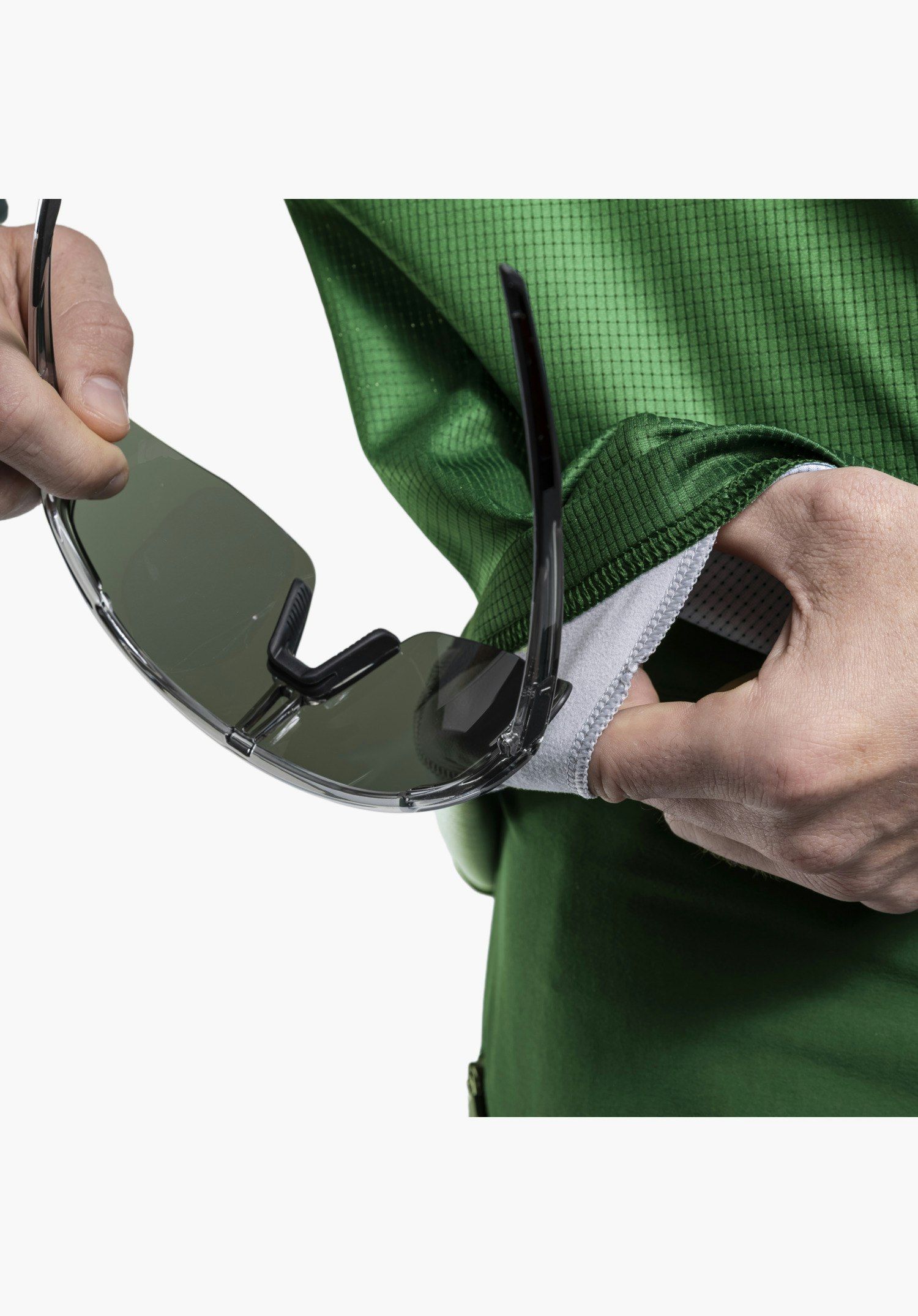 Longsleeve Style Koitere MEN in green. The image highlights the integrated glasses wipe on the inside of the hem being used to clean a pair of sports sunglasses, shown in a close-up against a white/neutral background.