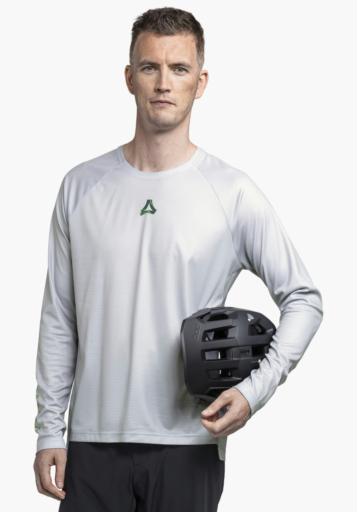 Longsleeve Style Koitere MEN in Grau. Ein Model steht frontal vor einem neutralen Hintergrund und präsentiert das Longsleeve, während es einen Helm unter dem Arm hält. Das markante Schöffel-Logo ist gut sichtbar im Brustbereich platziert.