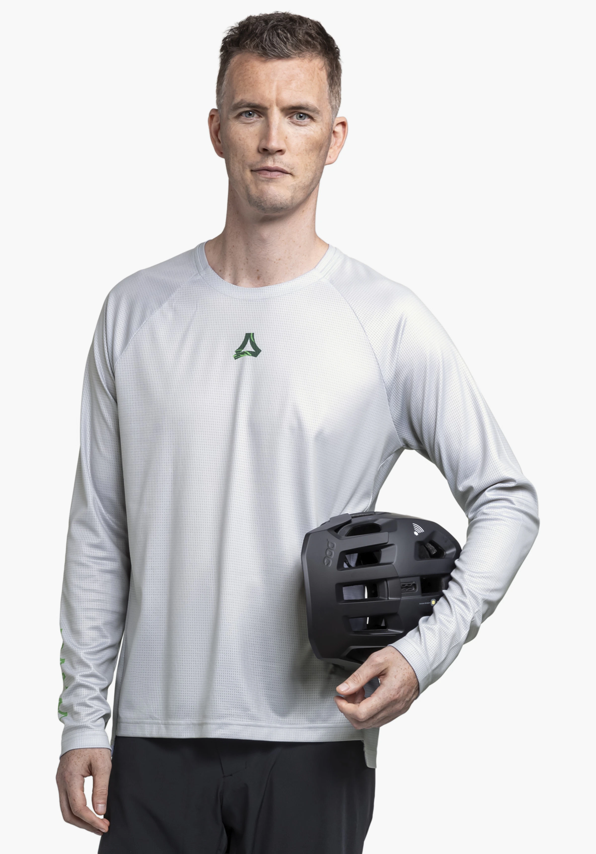 Longsleeve Style Koitere MEN in Grau. Ein Model steht frontal vor einem neutralen Hintergrund und präsentiert das Longsleeve, während es einen Helm unter dem Arm hält. Das markante Schöffel-Logo ist gut sichtbar im Brustbereich platziert.