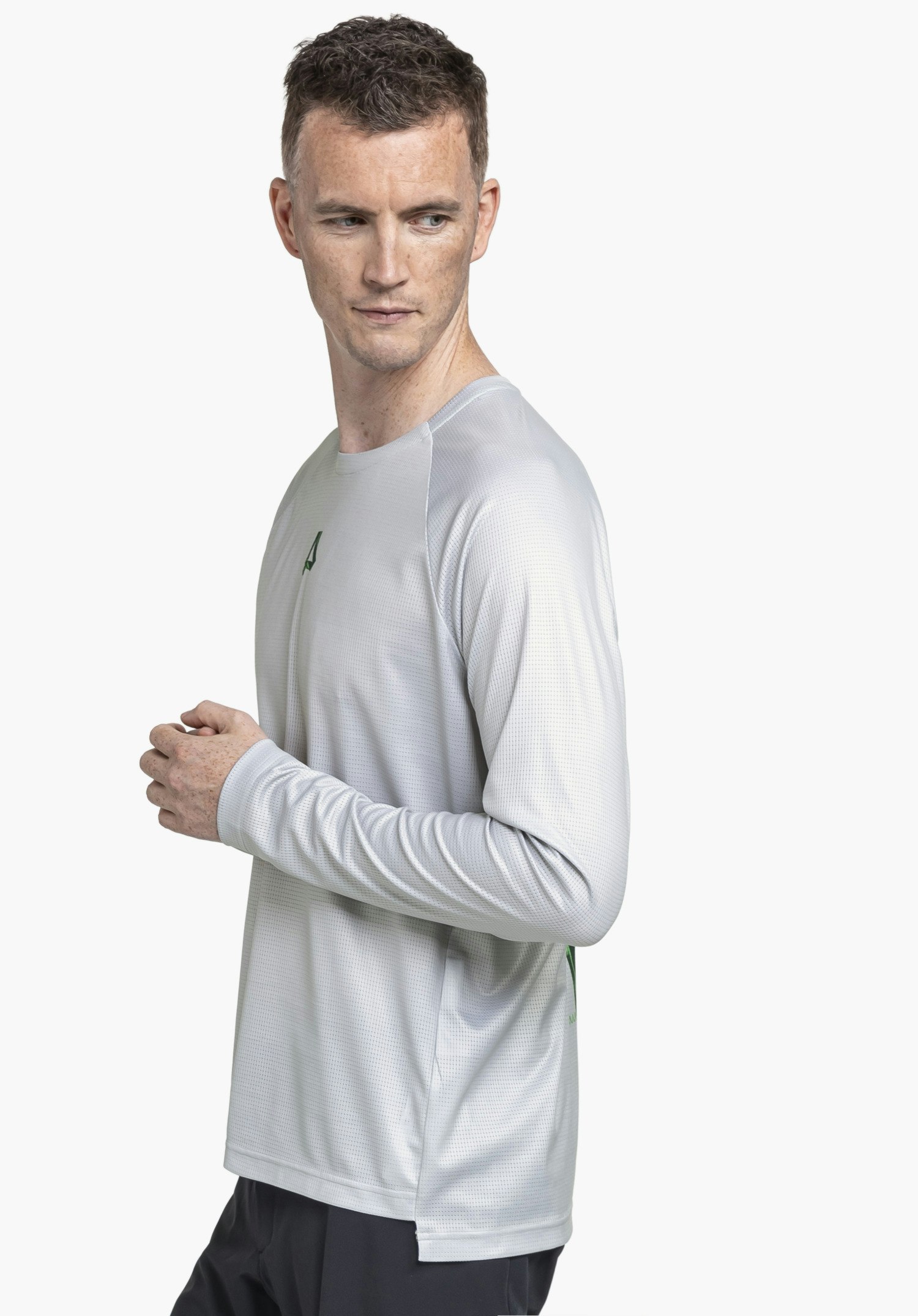 Longsleeve Style Koitere MEN in Grau: Ein Model steht seitlich vor einem neutralen Hintergrund und blickt zur Seite. Das Longsleeve überzeugt durch die cleane Passform, während das kleine Schöffel-Logo auf der Brust einen sportlichen Akzent setzt.