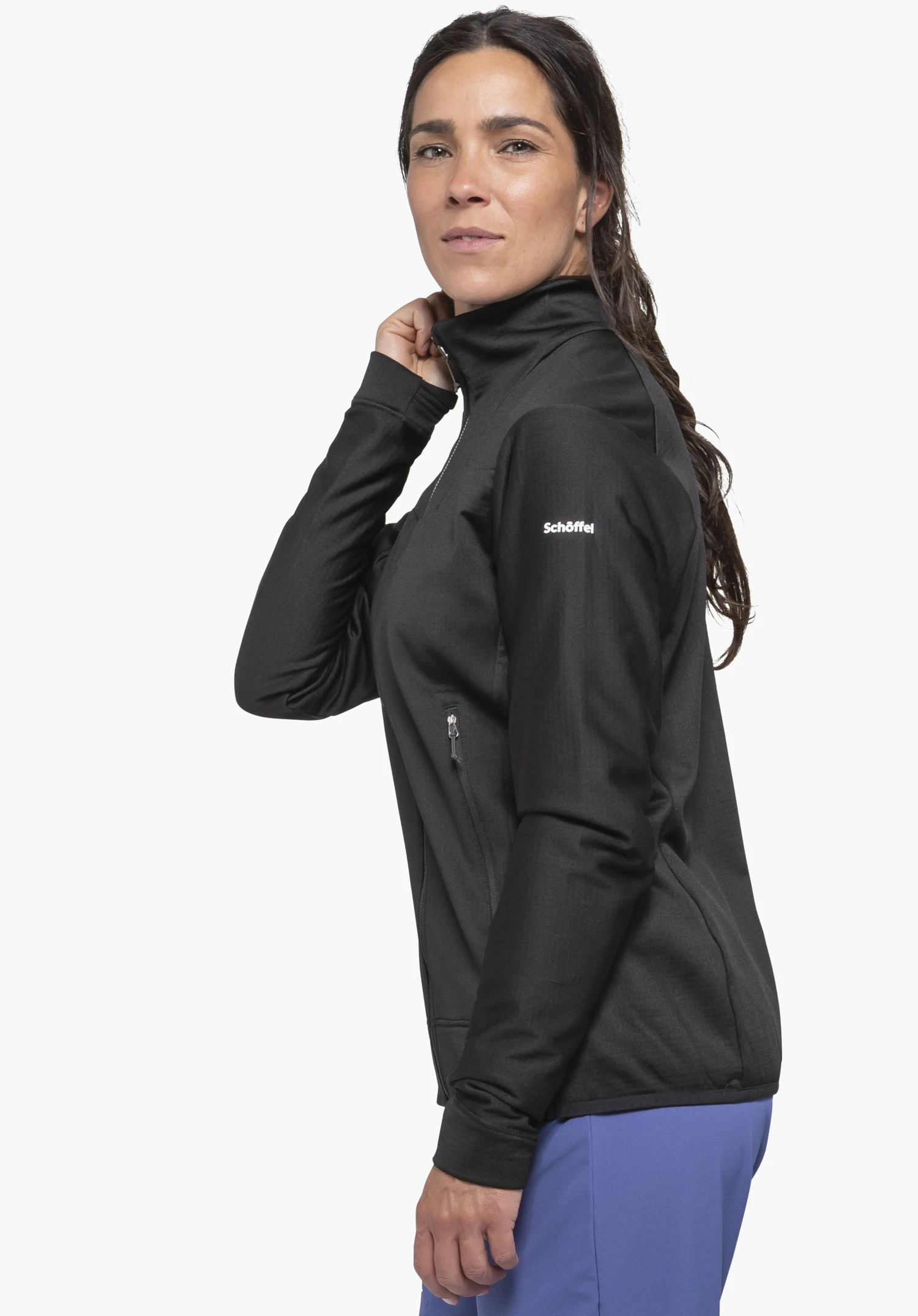 Fleece Jkt Style Blaueis WMS. Une femme porte la veste polaire noire en vue de profil sur un fond neutre. Sa main est posée sur le col, mettant en valeur le logo Schöffel blanc sur le haut du bras.