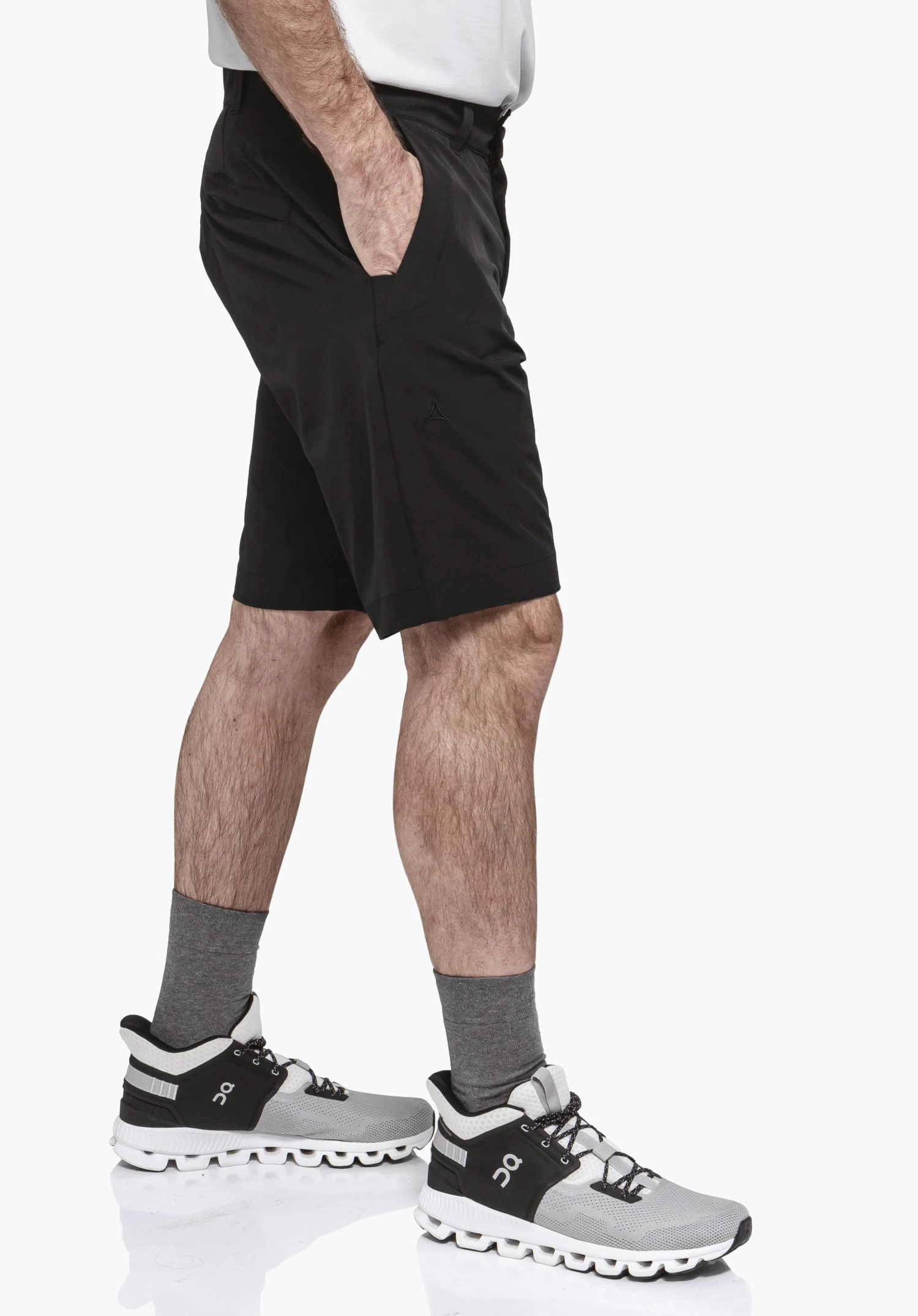 Shorts Style Gharra MNS in Schwarz: Ein Model steht seitlich vor einem neutralen Hintergrund und präsentiert die Passform der Hose. Das dezente Schöffel-Logo ist am linken Bein dezent platziert, während die Hand in der Tasche den funktionalen Alltagskomfort unterstreicht.