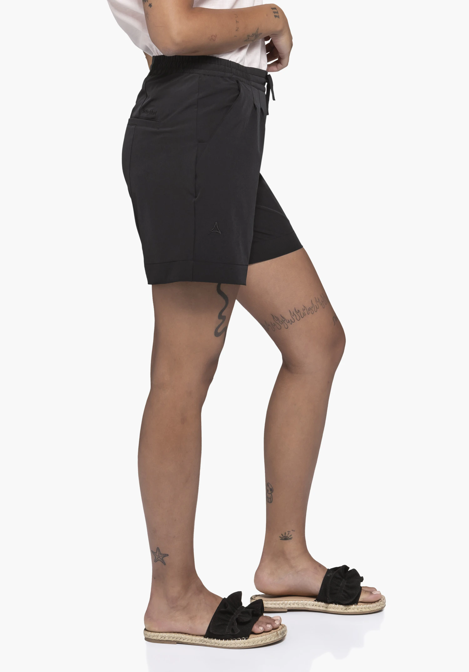 Shorts Style Gharra WMS en noir. Un mannequin se tient de profil et porte le short avec une taille élastique, un cordon de serrage et un logo Schöffel visible sur la jambe, sur un fond neutre.