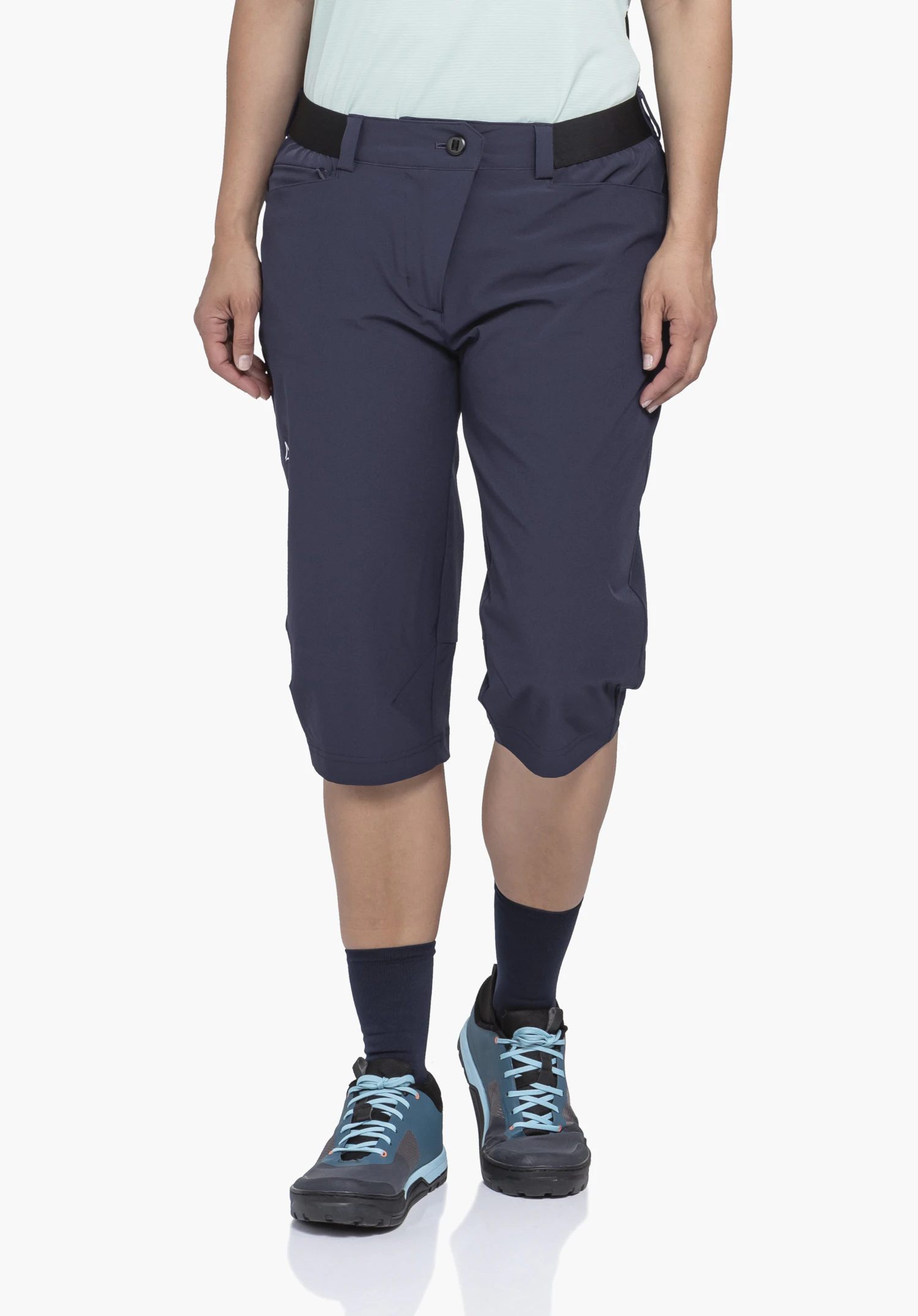 Capri Pants Style Keitele WMS in blue, worn by a model standing frontally and taking a slight step forwards. The white Schöffel logo is visible on the side of the right leg, presented against a neutral background.