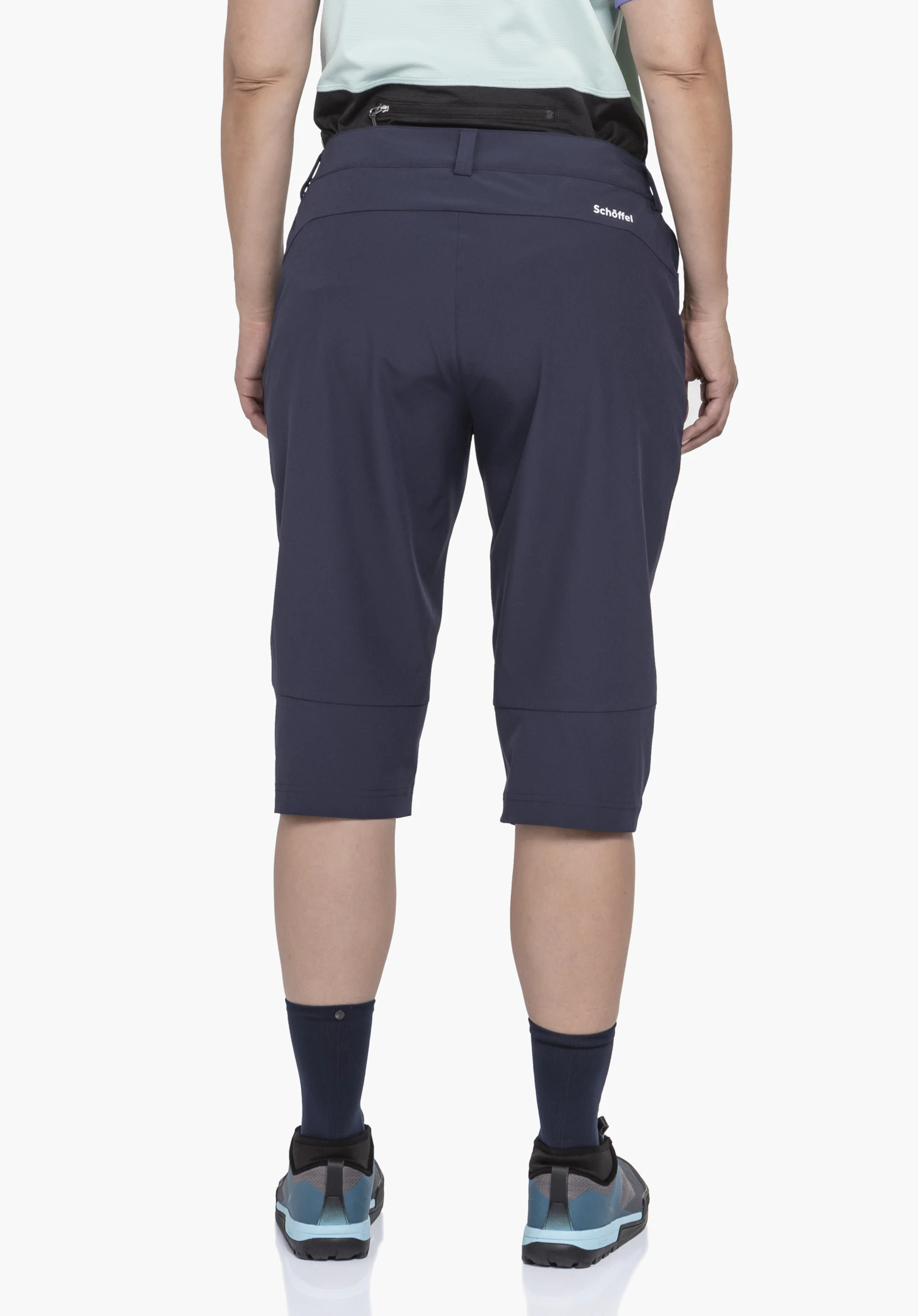 Capri Pants Style Keitele WMS in Blau, getragen von einem Model in der Rückenansicht. Die Hose zeigt das weiße Schöffel-Logo hinten rechts unterhalb des Bundes und wird vor einem neutralen Hintergrund präsentiert.