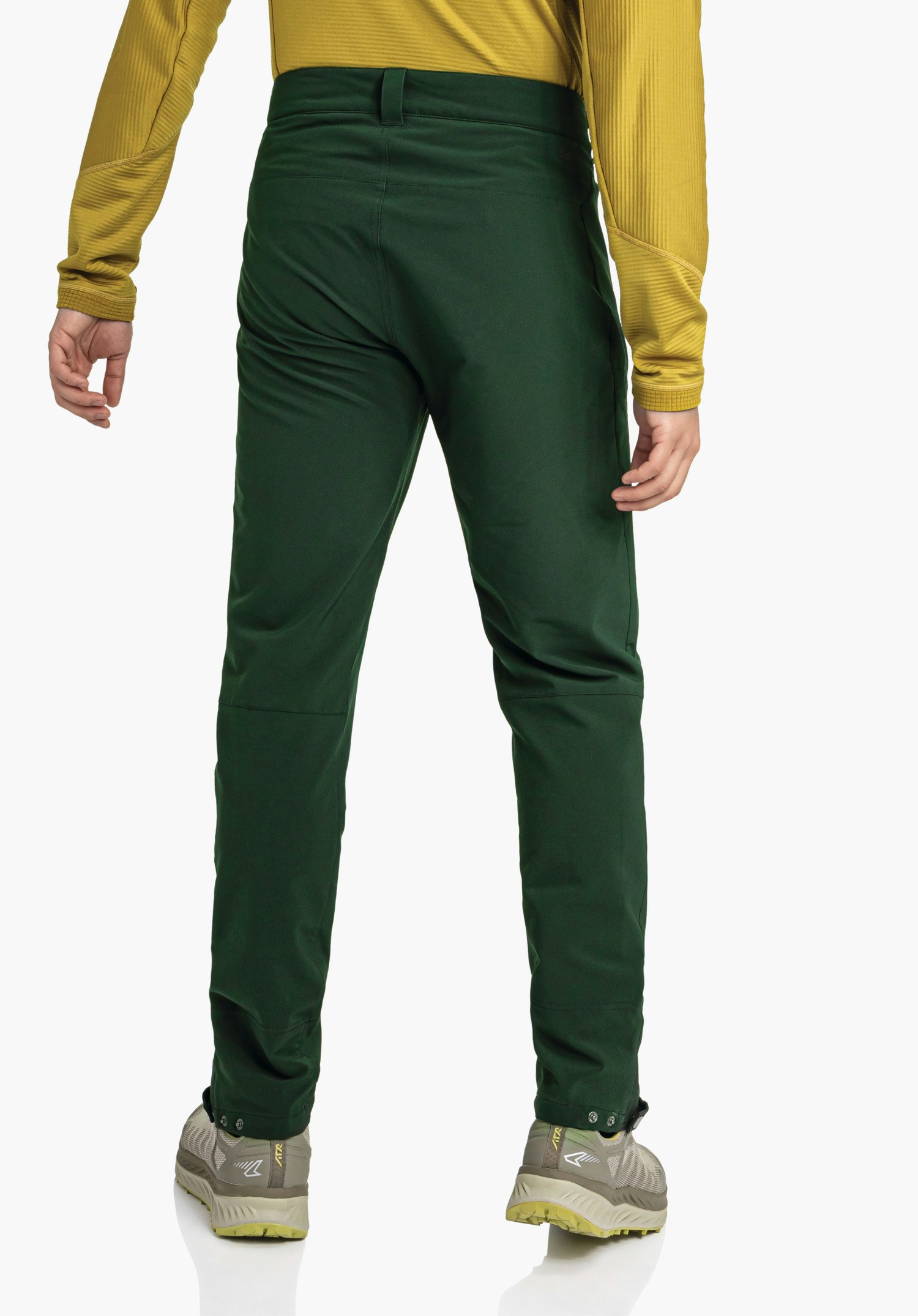 Pants Style Cascata MNS dark green trousers worn from the back; person standing with relaxed hands, wearing a dark yellow top and hiking shoes; white studio background.