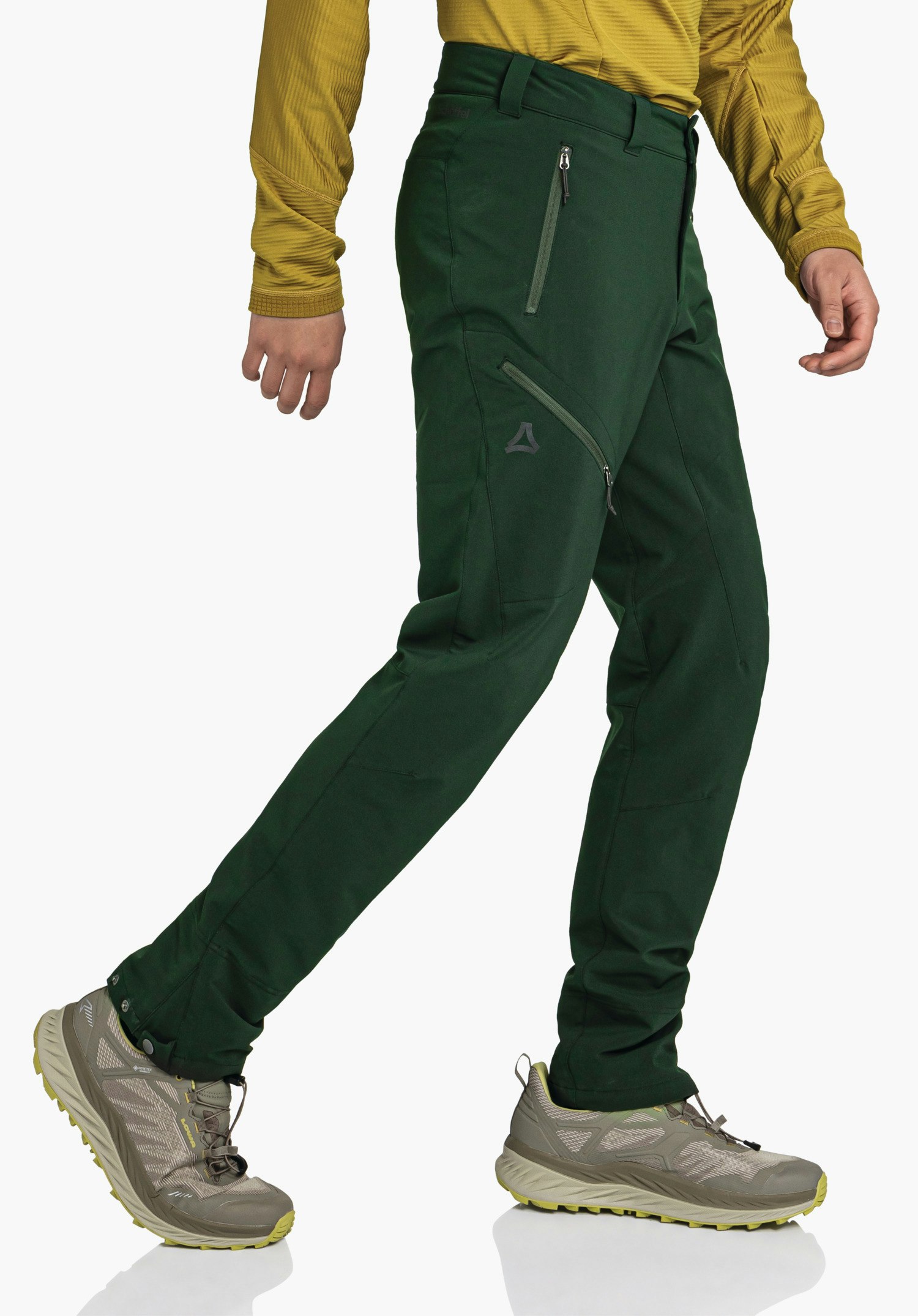 Pants Style Cascata MNS dark green hiking trousers in a stepping stance with Schöffel logo on the thigh; person wears a light yellow top and grey hiking boots with light yellow soles in front of a white background.