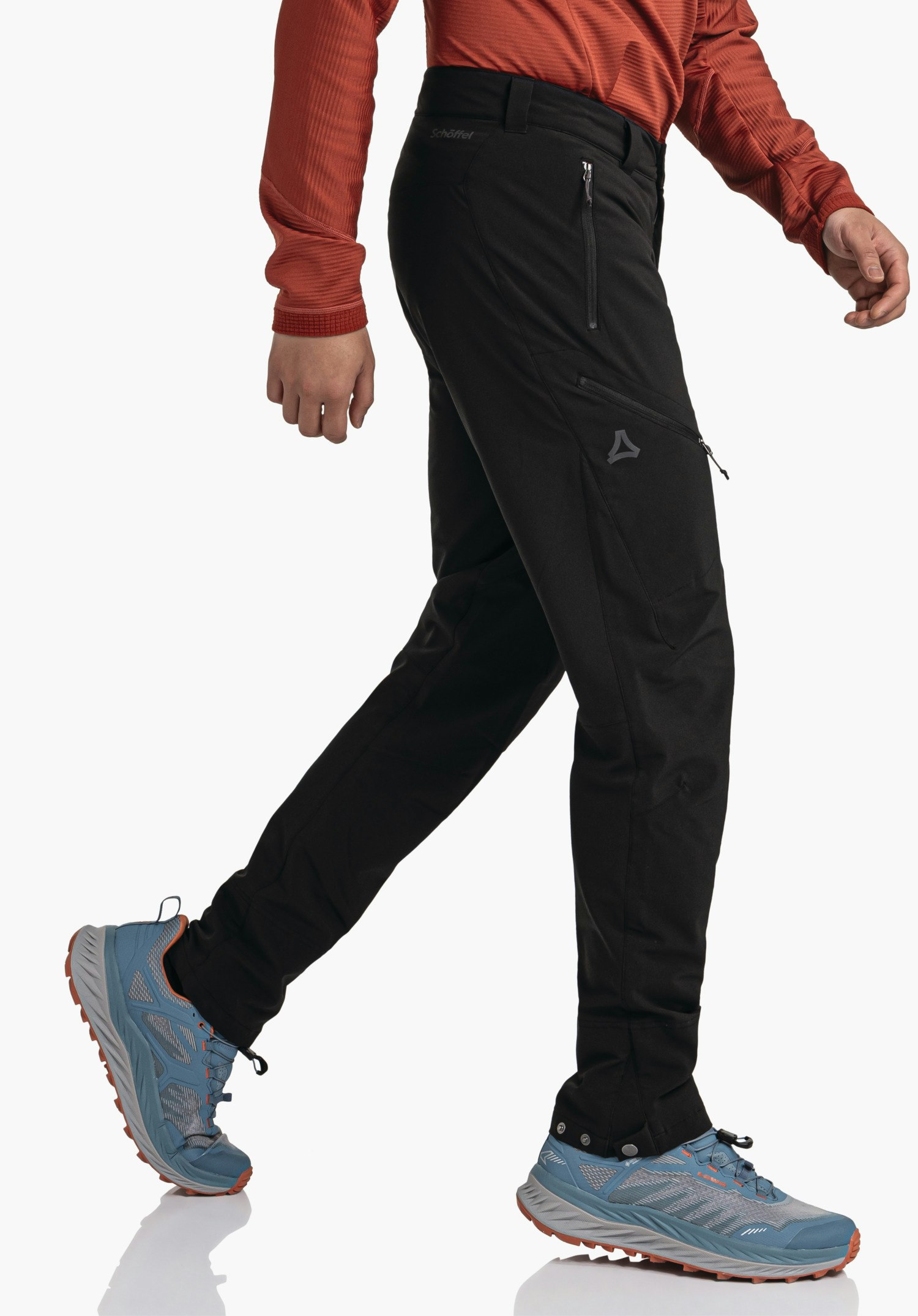 Pants Style Cascata MNS Schwarz Outdoorhose geht vor weißem Studiohintergrund, Person macht Schritt, trägt rot langärmeliges Oberteil und hellblau Schuhe; Schöffel-Logo sowie Text "Schöffel" sichtbar.