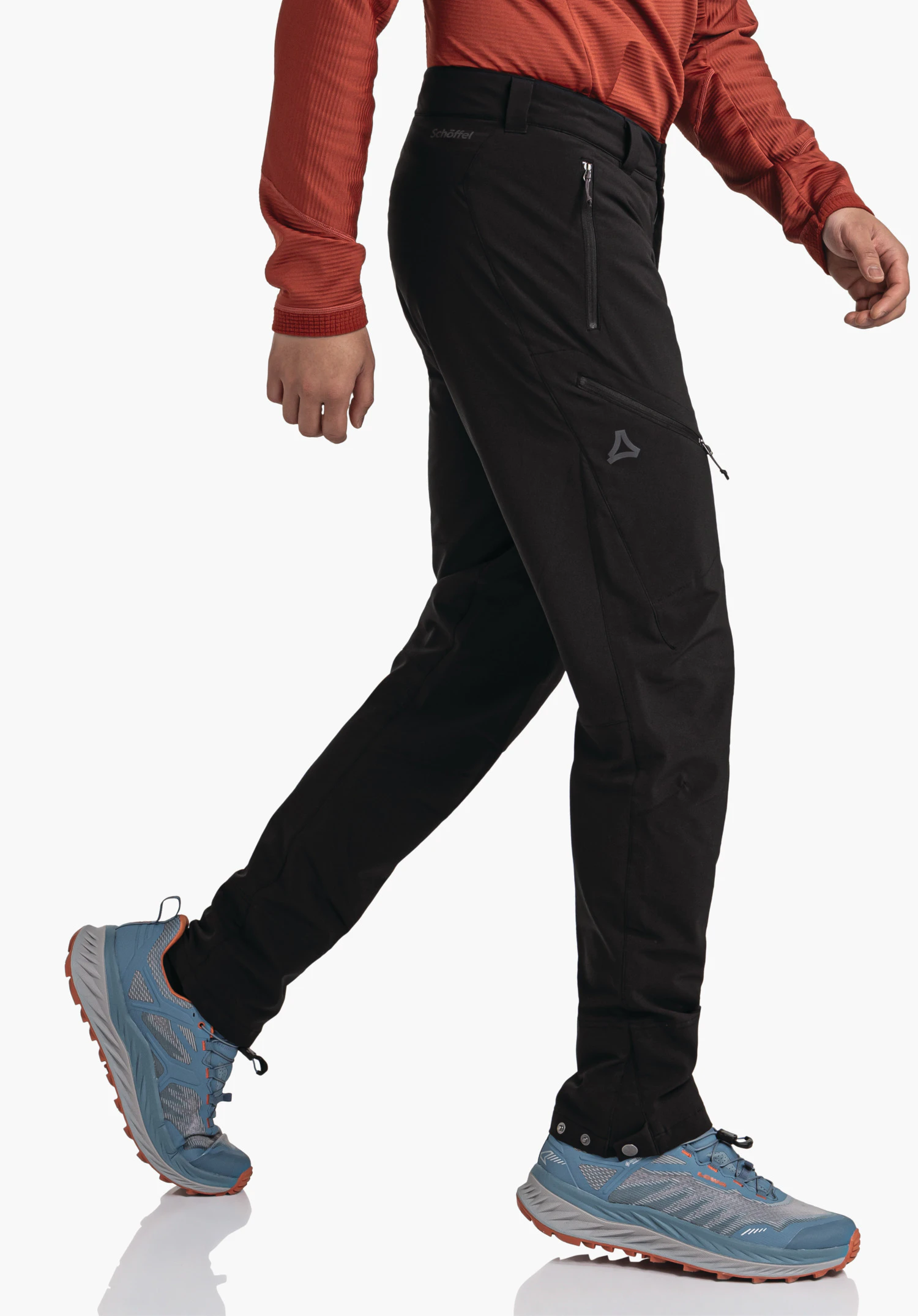 Pants Style Cascata MNS black outdoor trousers walking in front of a white studio background; person takes a step, wears a red long-sleeve top and light blue shoes; Schöffel logo and text "Schöffel" visible.