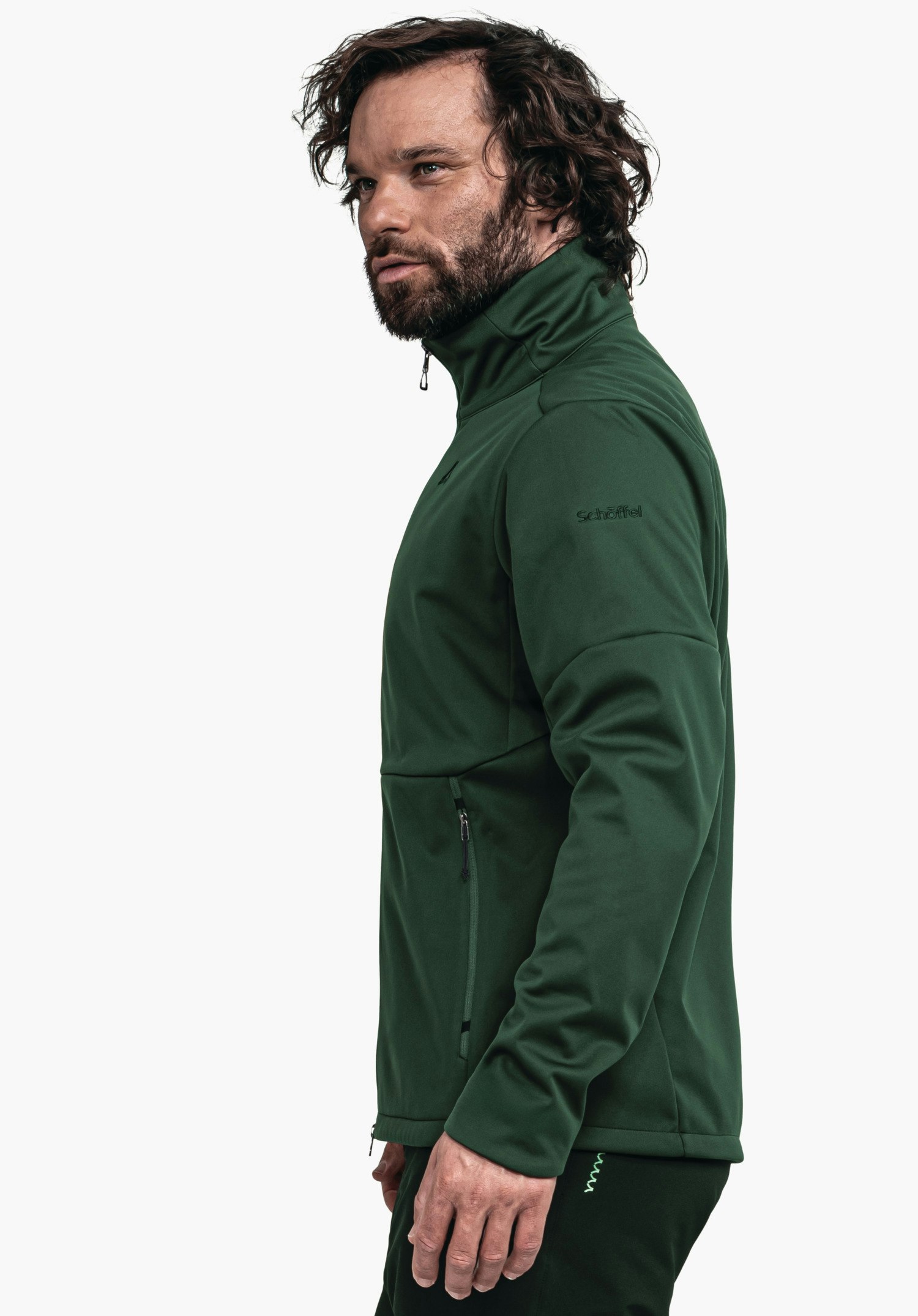 Softshell Jk Style Fracon MNS Dunkelgrüne Jacke wird von einem stehenden Mann getragen, Kragen hochgezogen, seitliche Reißverschlusstasche sichtbar; neutraler weißer Hintergrund. Text: "Schöffel".