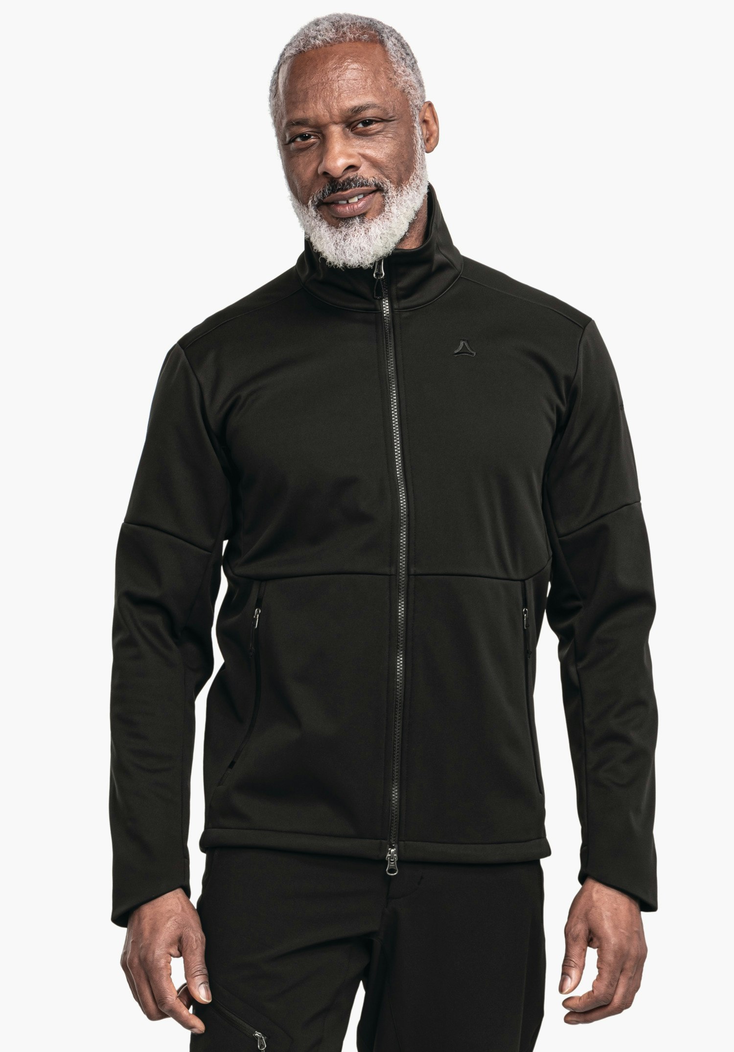 Softshell Jk Style Fracon MNS schwarze Reißverschlussjacke: Person steht frontal, trägt Jacke mit Schöffel-Logo auf der Brust, leichtes Lächeln, weißer Bart, entspannte Haltung, neutraler weißer Studiohintergrund.