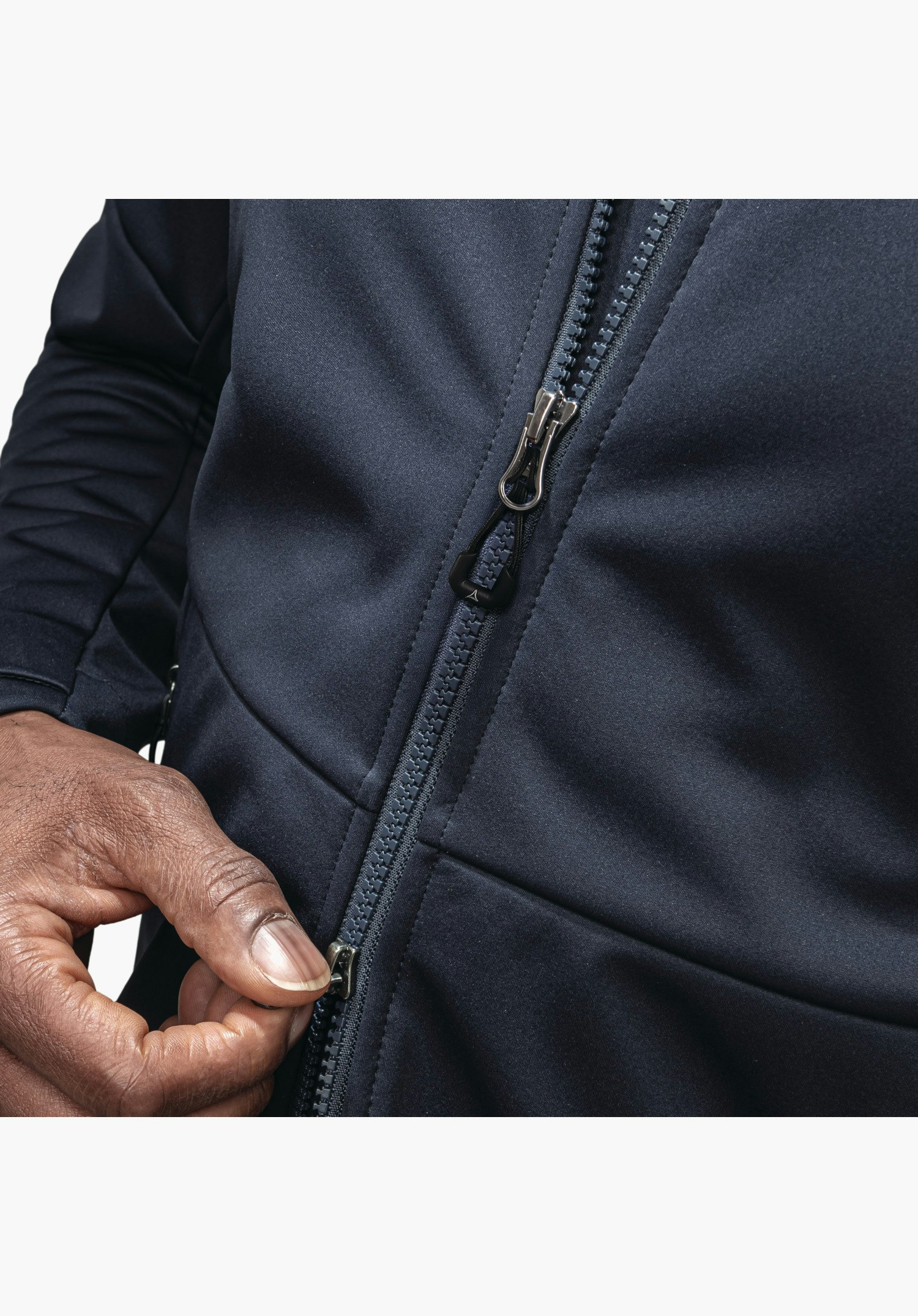 Softshell Jk Style Fracon MNS, detailed view of the robust front zip with Schöffel logo on the zip pull against the blue technical fabric, with a hand adjusting the fastening, close-up against a white/neutral background.