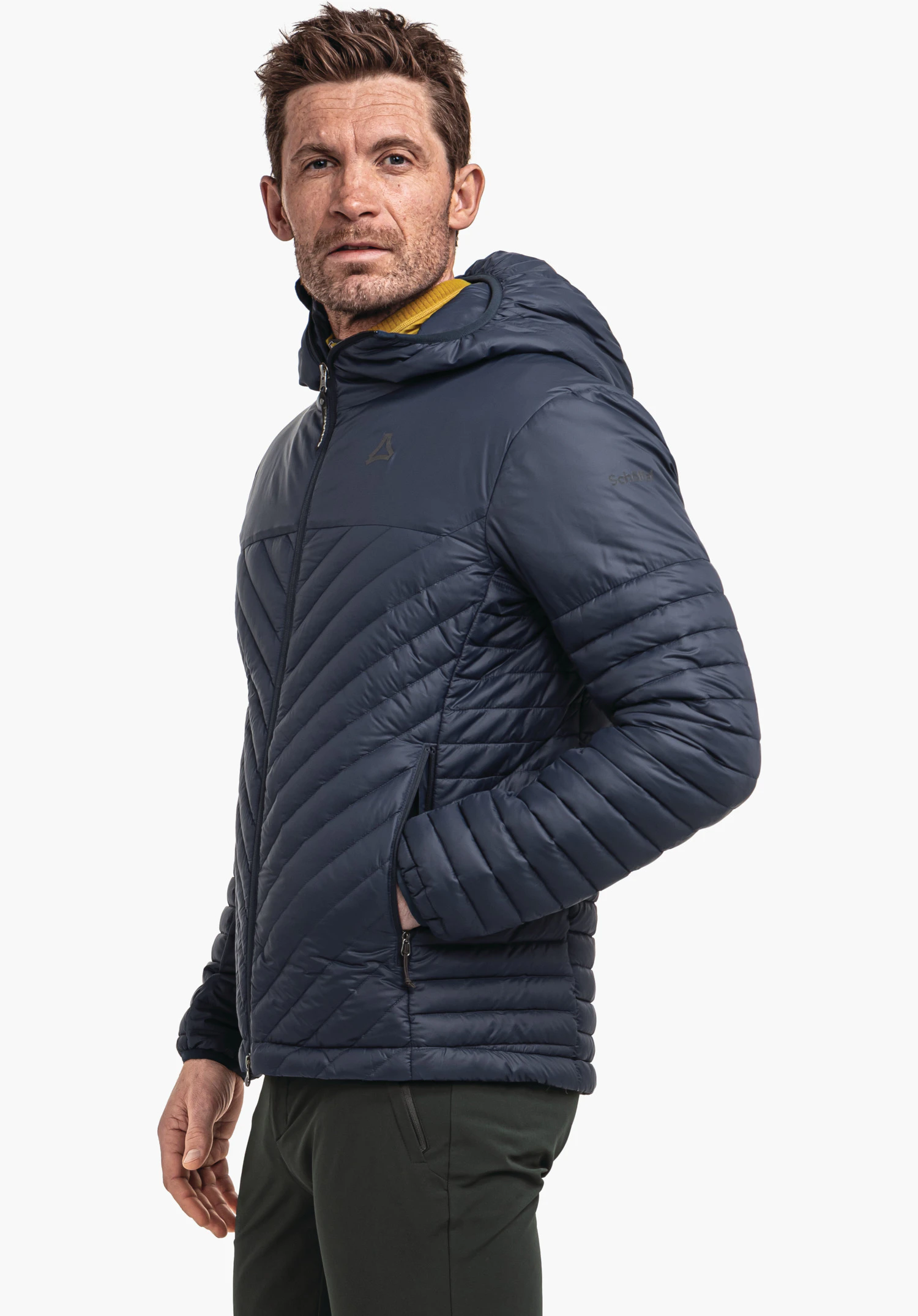Down Jacket Style Cascata MNS Dunkelblaue Steppjacke mit Kapuze (Schöffel-Logo) getragen von einem Mann; rechte Hand in Tasche; hellgelber Kragen sichtbar; weißer Hintergrund. Text: "Schöffel".