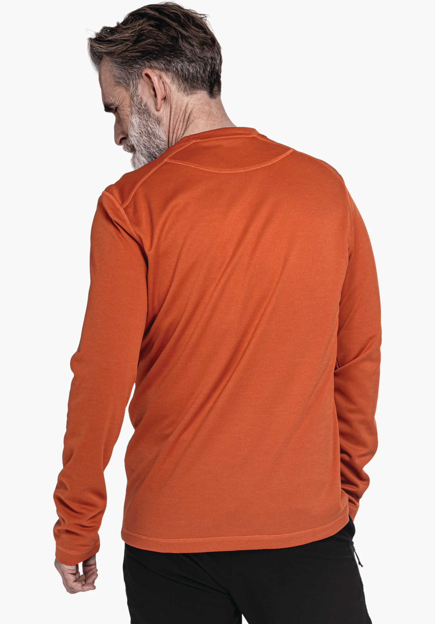 CIRC Longsleeve Style Smue MNS haut à manches longues orange, porté par un homme debout regardant par-dessus l’épaule gauche; contexte: surface blanche, pantalon noir visible.