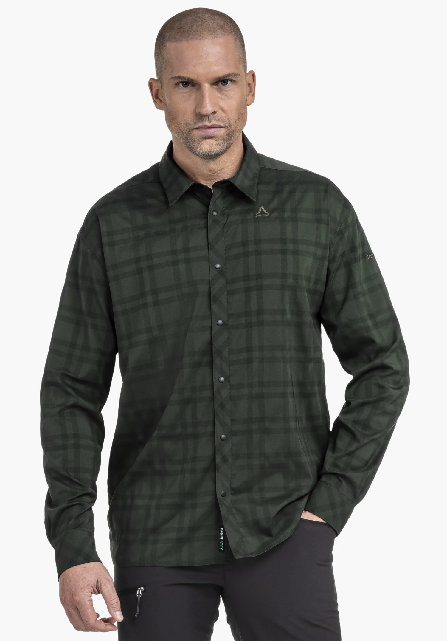 Shirt Style Yekuro MNS dark green checked long-sleeve shirt with button placket and Schöffel logo on the chest; model stands against a white background, right hand in trouser pocket.
