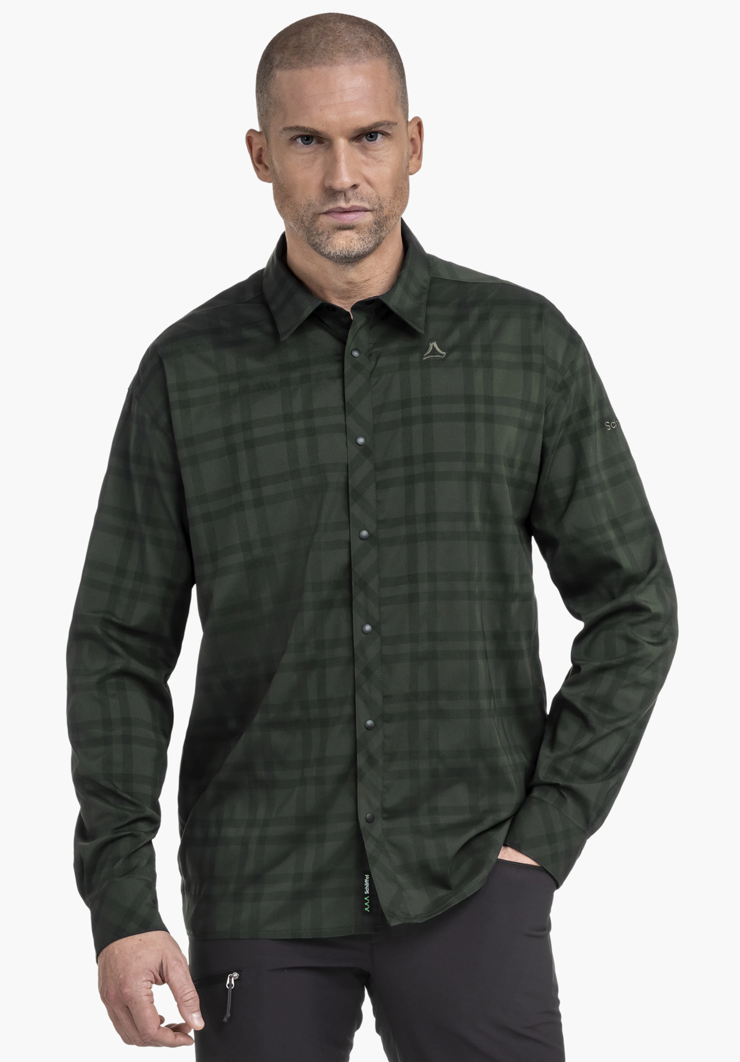 Shirt Style Yekuro MNS dark green checked long-sleeve shirt with button placket and Schöffel logo on the chest; model stands against a white background, right hand in trouser pocket.