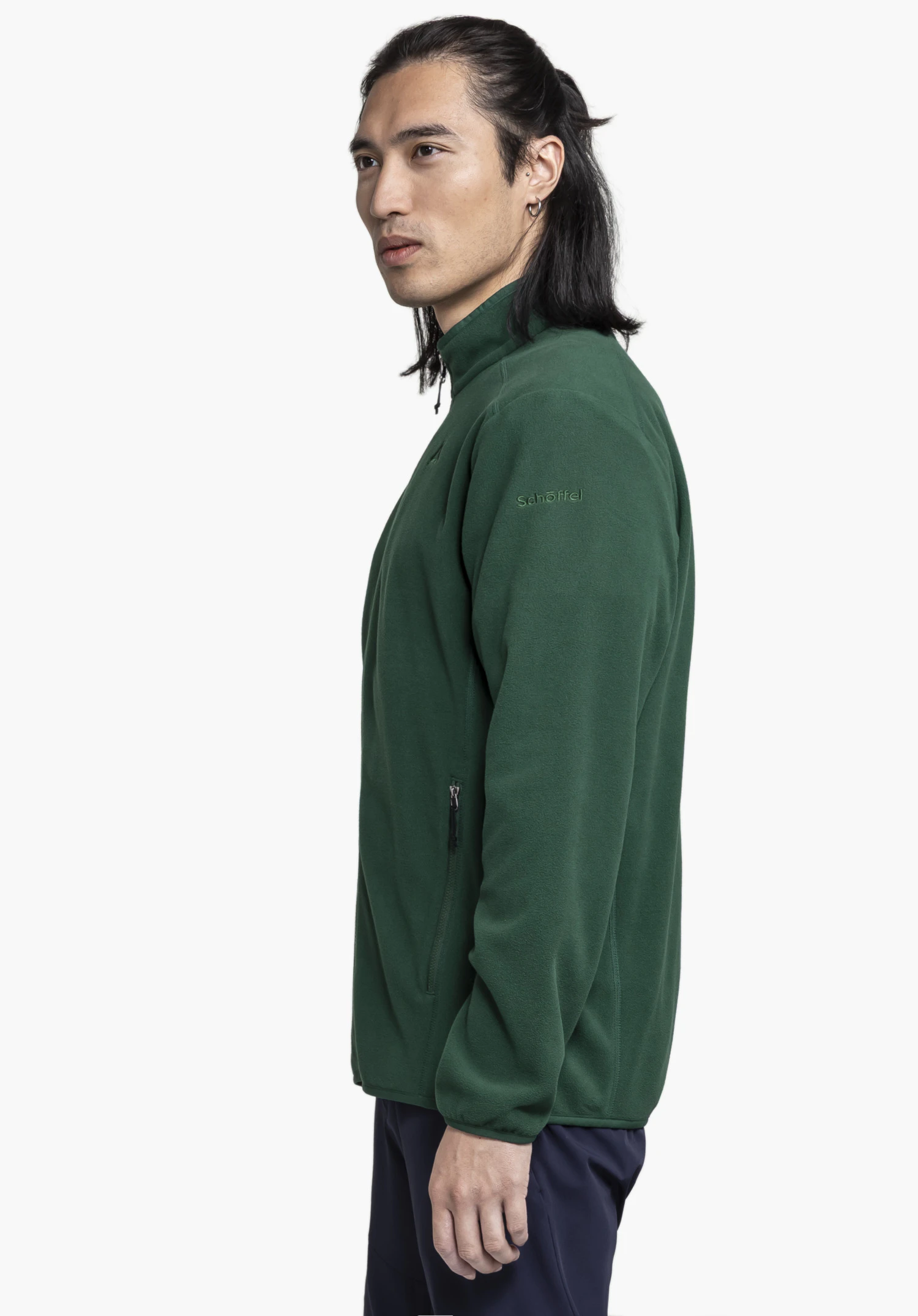 Fleece Jk Style Ash MNS : Un mannequin pose de profil devant un fond neutre pour présenter cette veste polaire en vert. Le logo Schöffel, discrètement brodé en vert sur le haut du bras, souligne le style épuré du modèle.