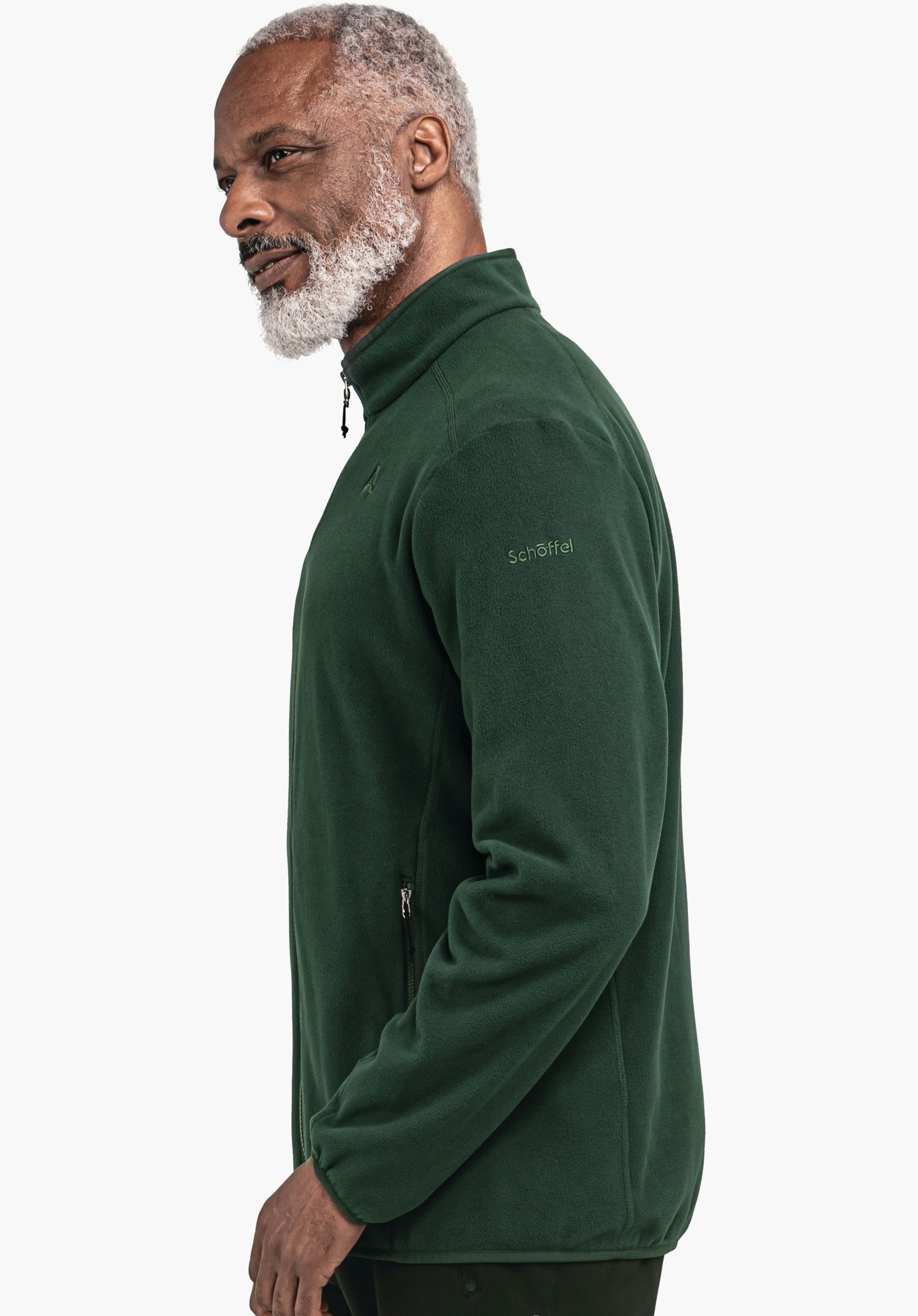 Fleece Jk Style Ash MNS Mann steht seitlich, trägt dunkelgrüne Fleecejacke mit Reißverschluss und der Aufschrift "Schöffel" am Ärmel; schaut nach vorn vor hellem, einfarbigem Hintergrund.