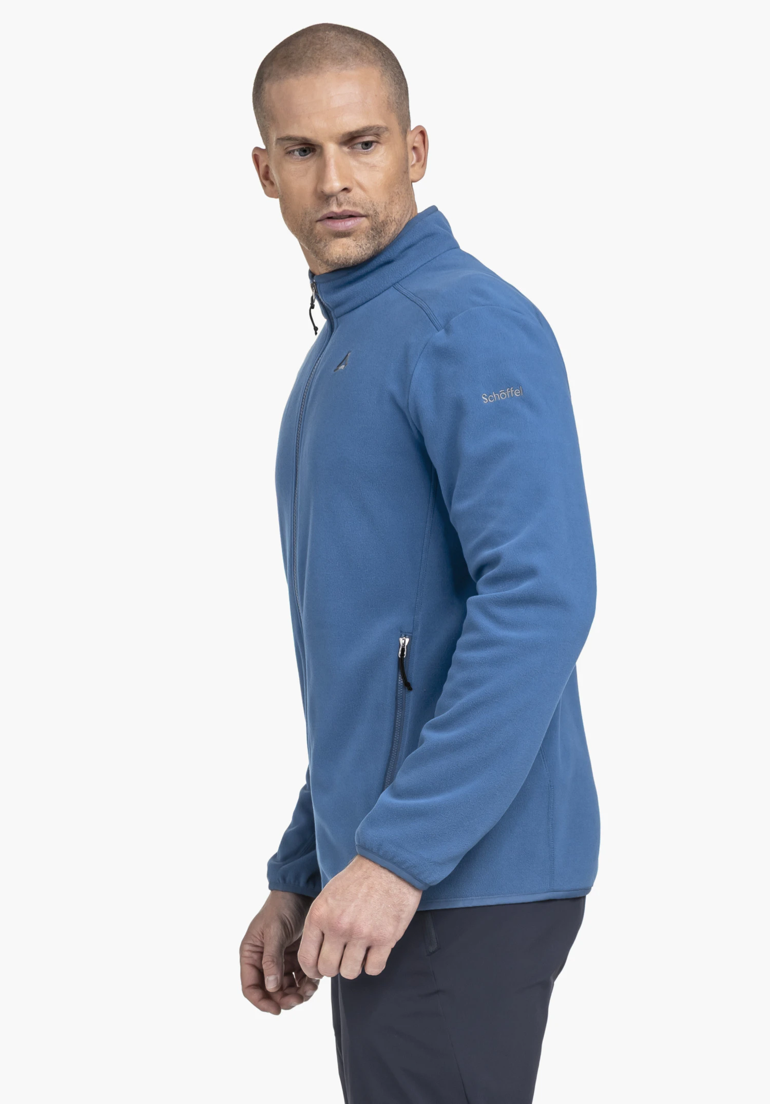 Fleece Jk Style Ash MNS en bleu : Un mannequin se tient de profil devant un fond neutre et présente la veste en polaire. Le logo Schöffel discret est clairement visible sur la manche.
