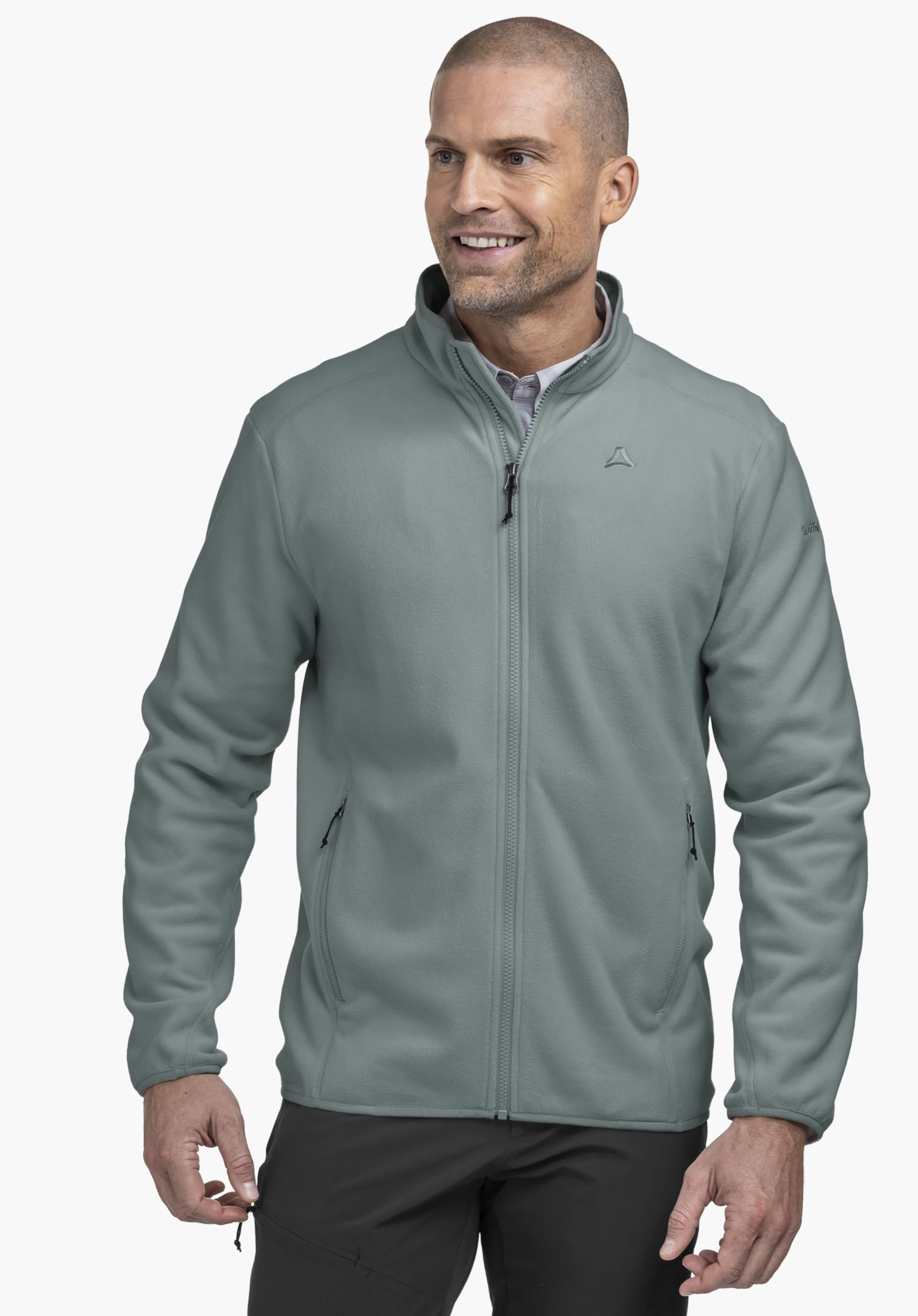 Fleece Jk Style Ash MNS worn by a model standing frontally and looking to the side. The grey fleece jacket with a visible Schöffel logo on the left chest is presented against a neutral background.