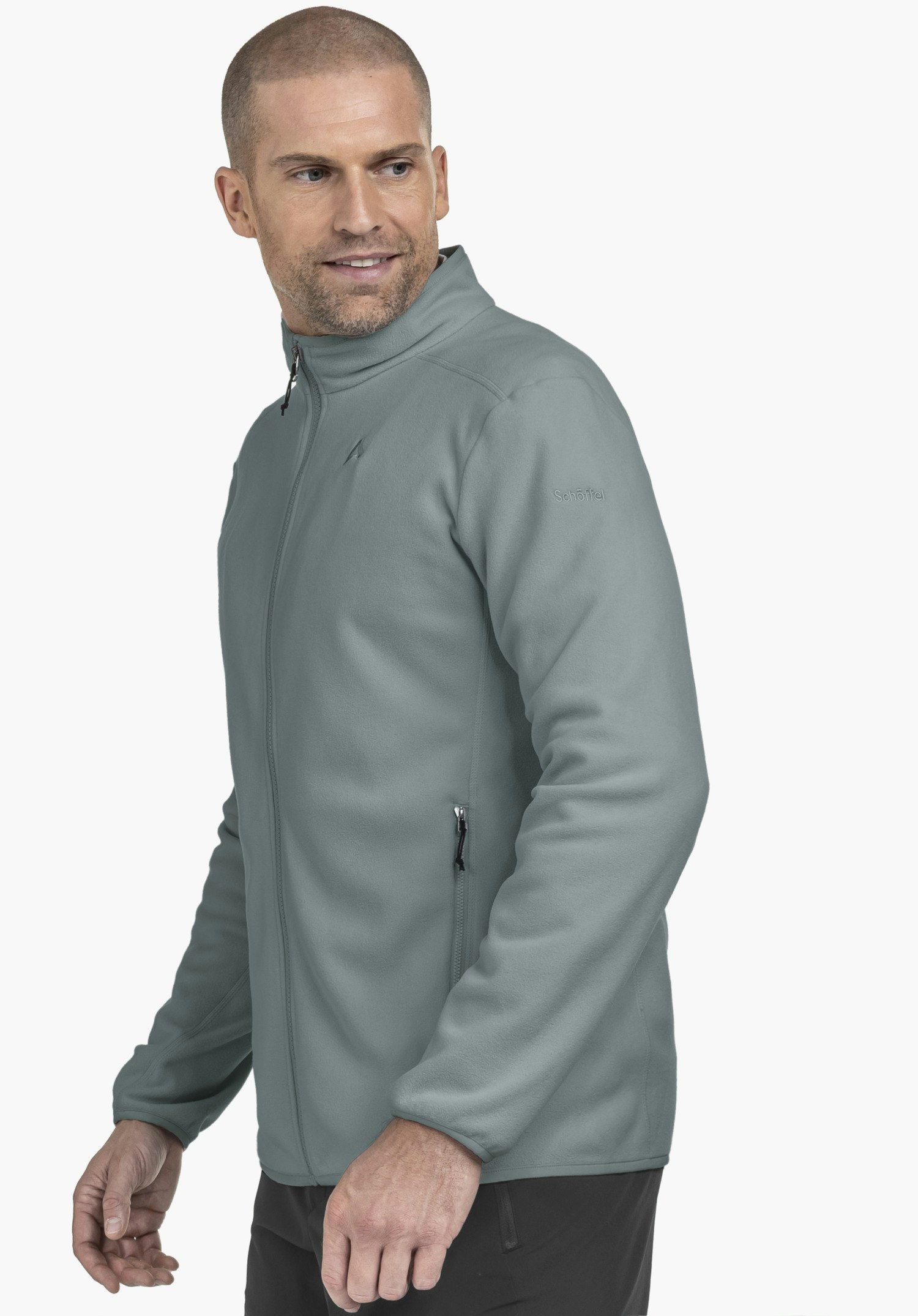 Fleece Jk Style Ash MNS in Grau. Ein Model steht seitlich vor einem neutralen Hintergrund und trägt die Jacke, wobei das diskrete Schöffel-Logo auf dem Oberarm gut zu erkennen ist.