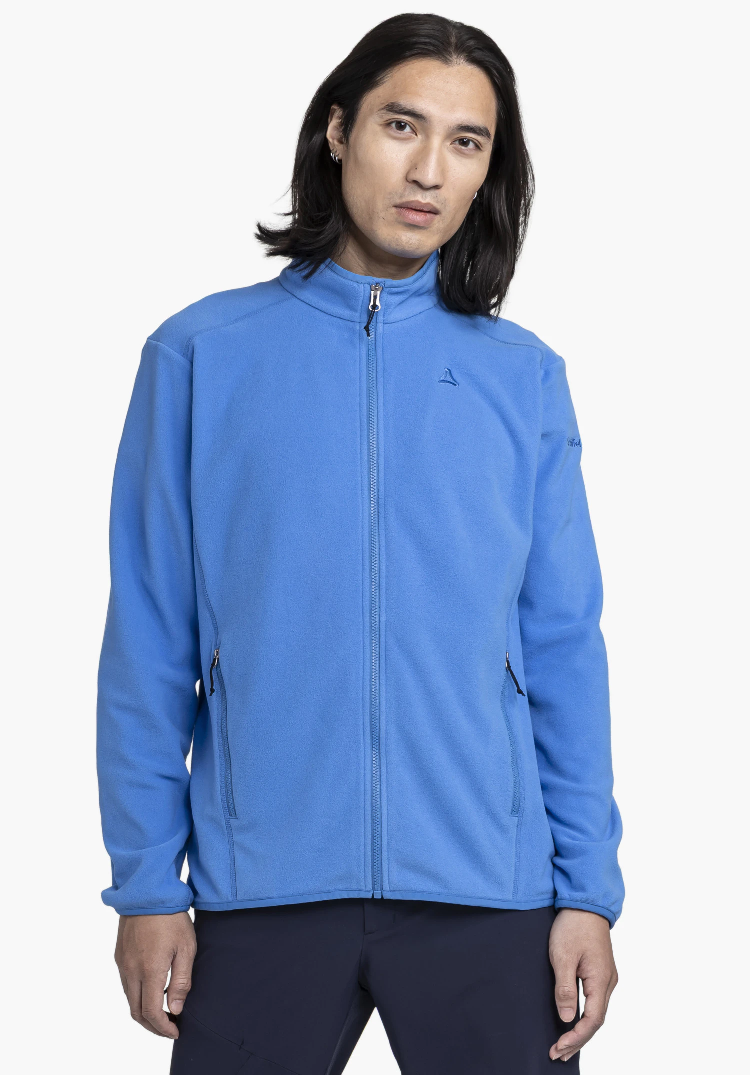 Fleece Jk Style Ash MNS is worn by a model standing in a frontal pose. The blue jacket features a closed zip and the Schöffel logo on the chest against a neutral background.