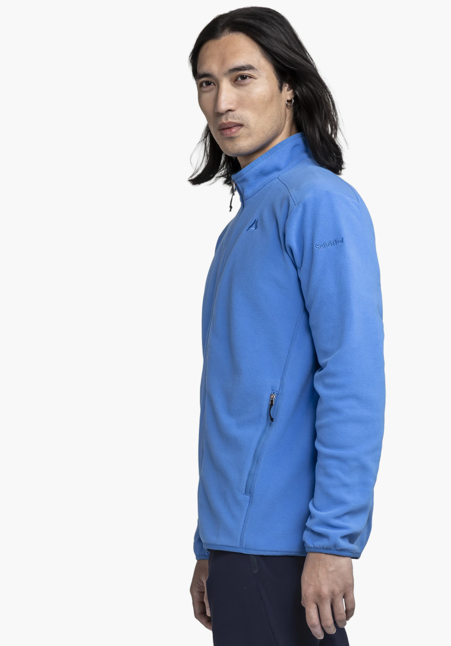 Fleece Jk Style Ash MNS: A male model stands sideways against a neutral background, showcasing the jacket in blue. He is looking directly at the camera, with the subtle Schöffel logo clearly visible on the upper arm.