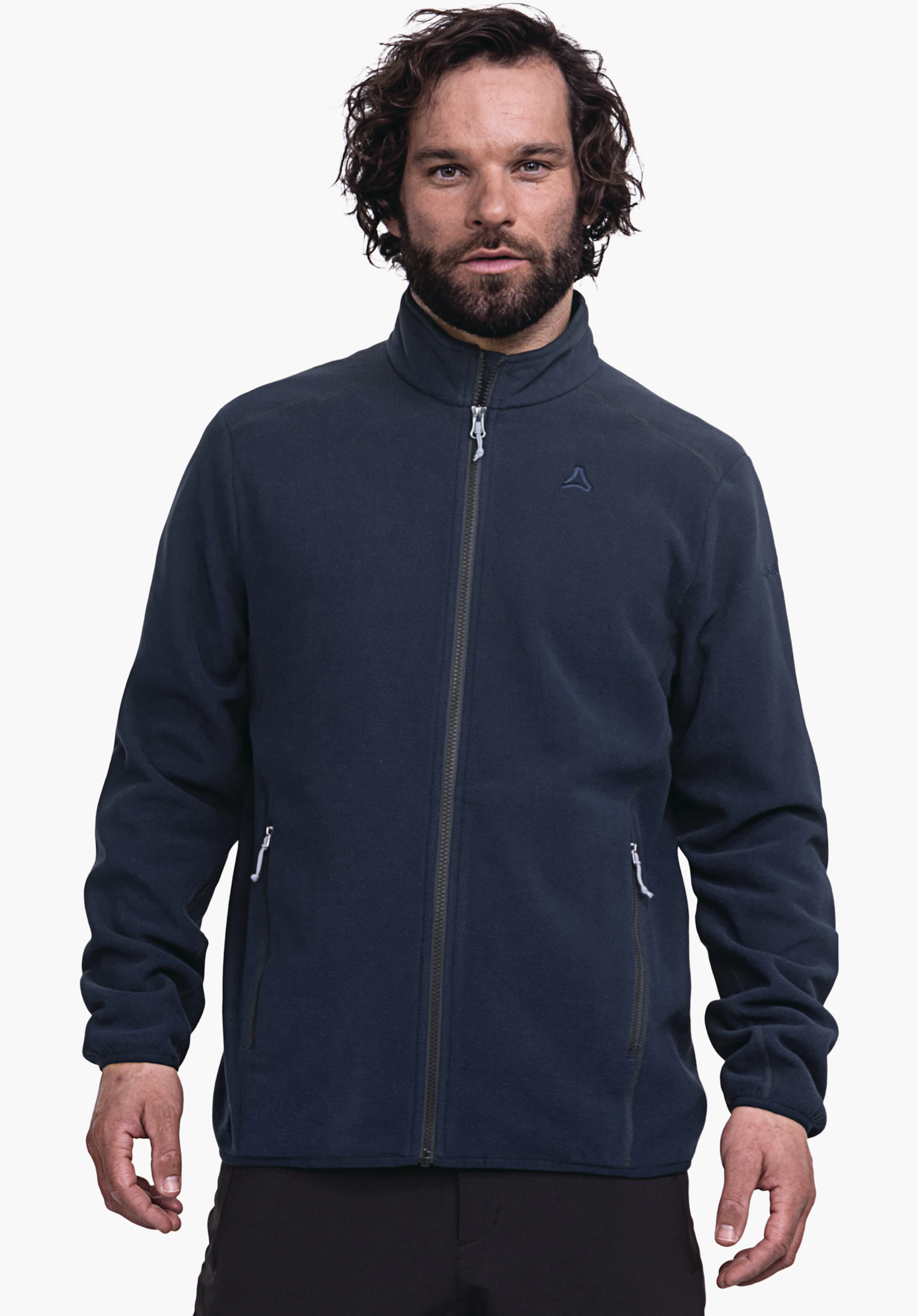 Fleece Jk Style Ash MNS veste polaire bleu foncé avec logo Schöffel, portée par un homme debout de face; fermeture éclair fermée, mains détendues dans les poches zippées; fond blanc.