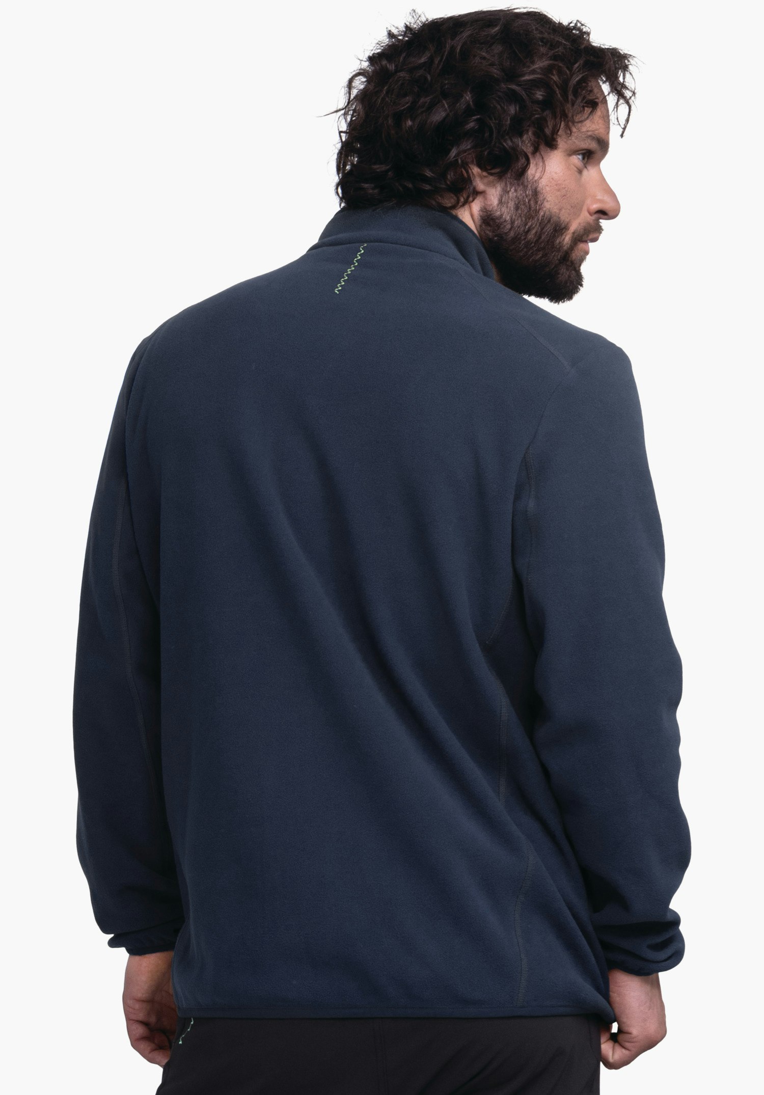 Fleece Jk Style Ash MNS Dunkelblaue Fleecejacke, getragen von einem Mann, der den Oberkörper dem Betrachter zuwendet und den Kopf nach rechts dreht; kleine hellgrüne Zickzacknaht am Nacken; heller Hintergrund.