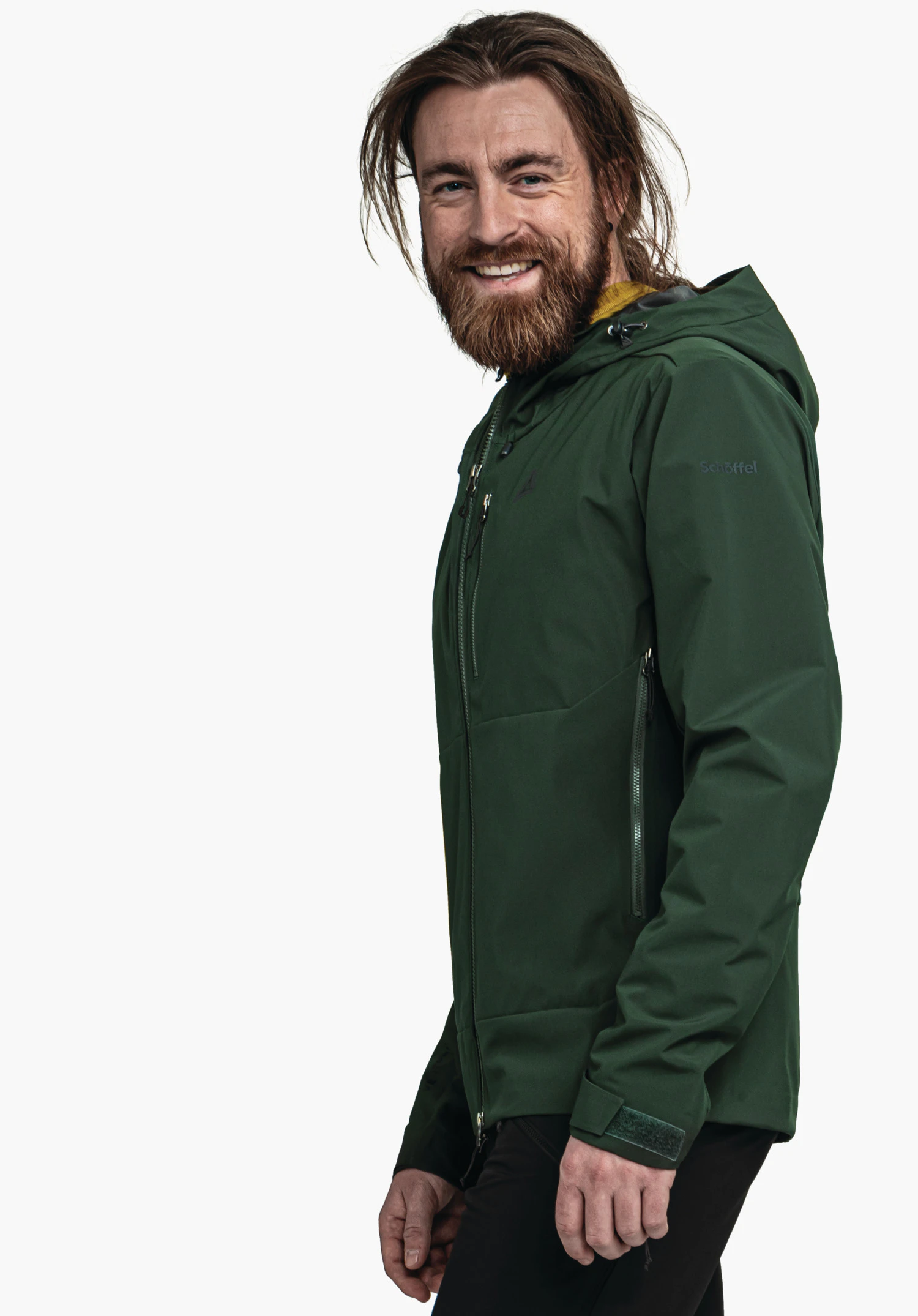 Softshell Jk Style Milagle MNS dunkelgrüne Jacke; Mann mit braunem Bart lächelt, trägt sie seitlich stehend mit Kapuze vor weißem Hintergrund. Text: "Schöffel". Schöffel-Logo sichtbar.
