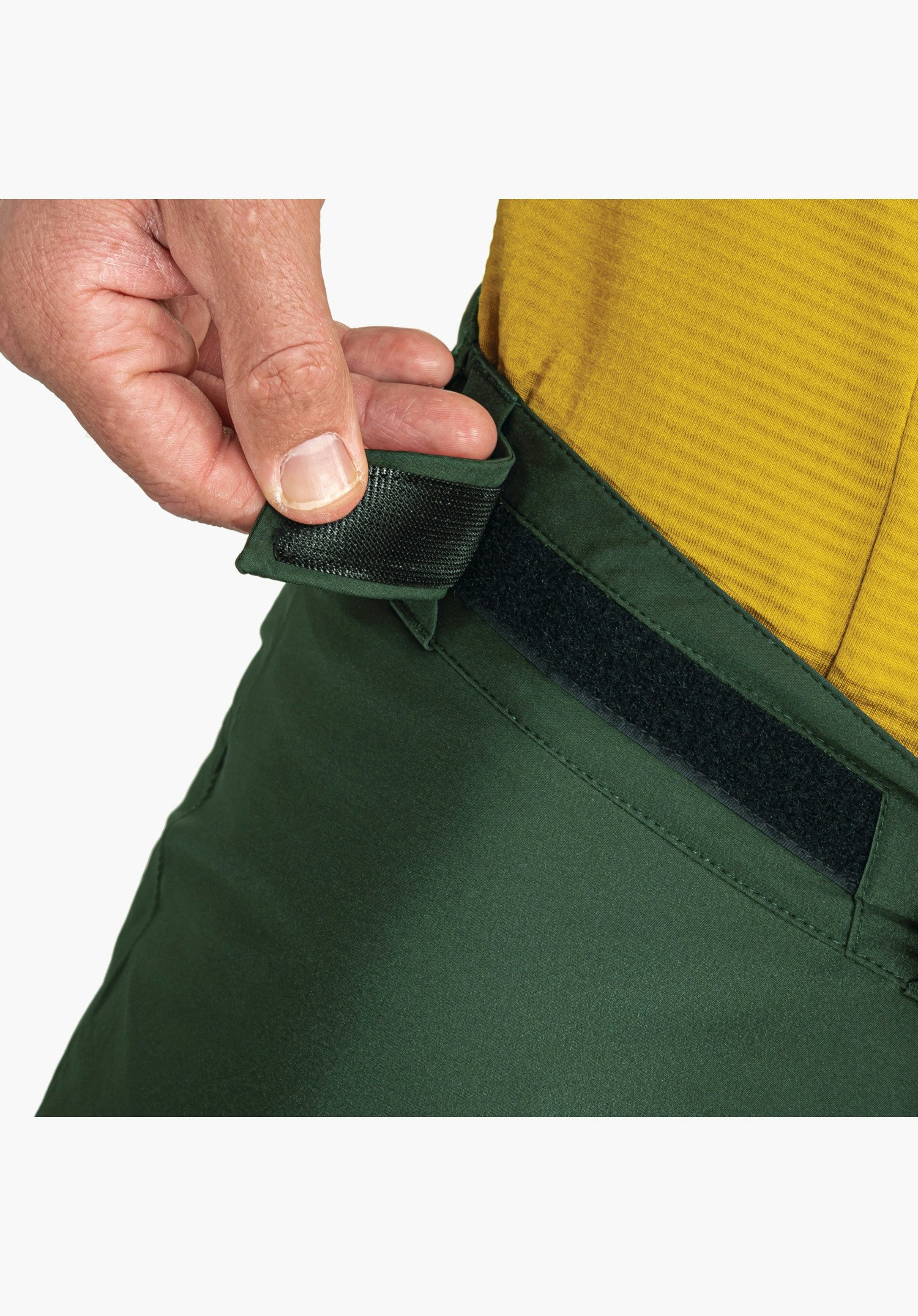 Pants Style Milagle MNS shows the adjustable waistband with velcro fastening on the green fabric as a hand adjusts the fit, close-up against a white background.