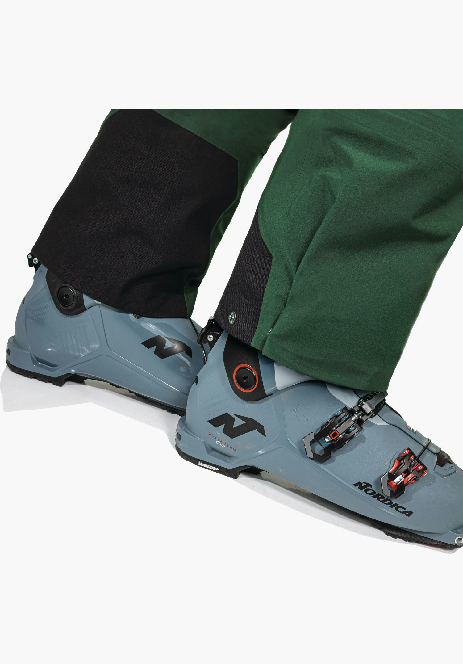 Pants Style Milagle MNS features the durable black edge protection at the bottom hem of the green leg, worn over ski boots. Close-up against a white background.